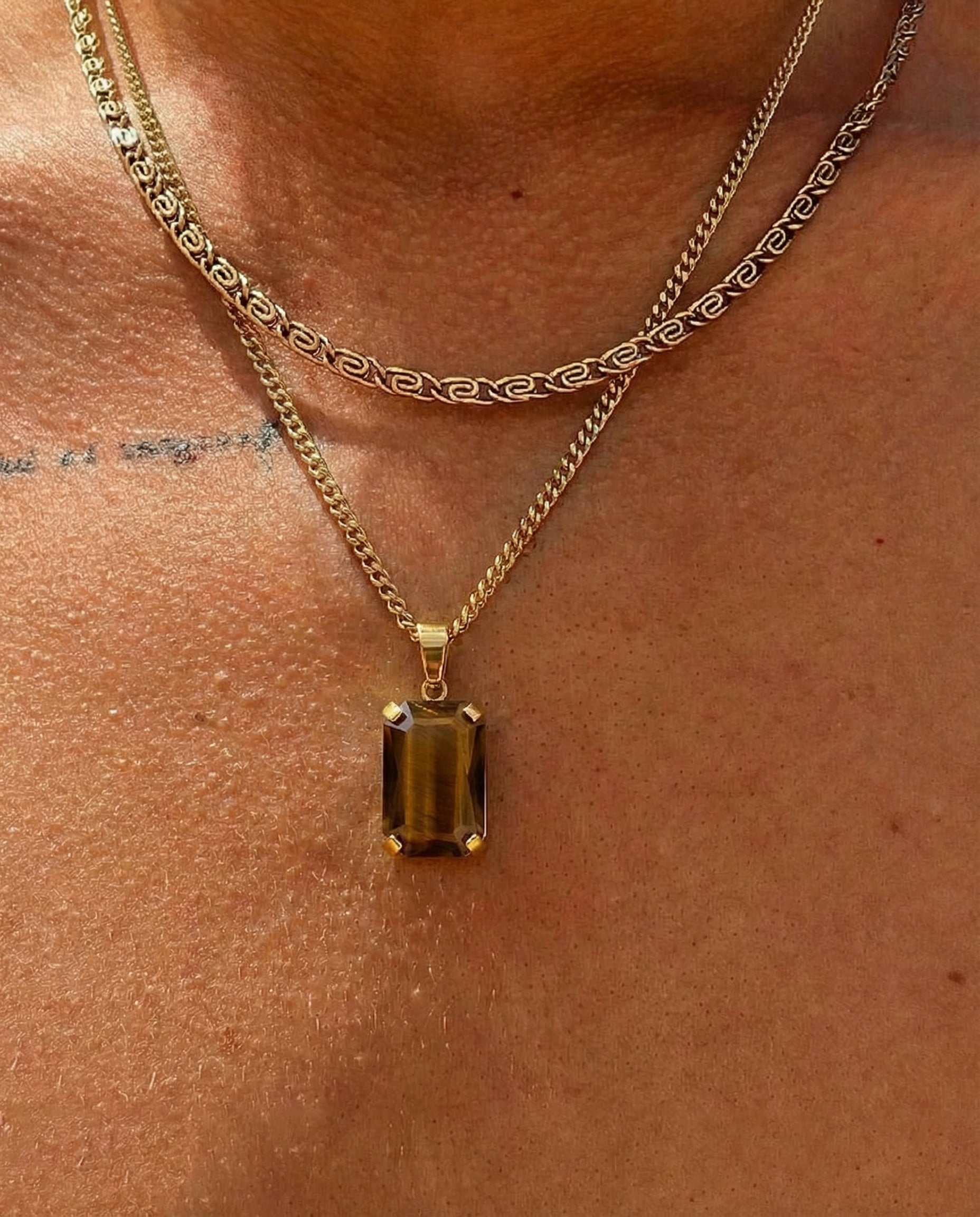Close up of a VOLT gold necklace on skin with a rectangular amber gemstone pendant