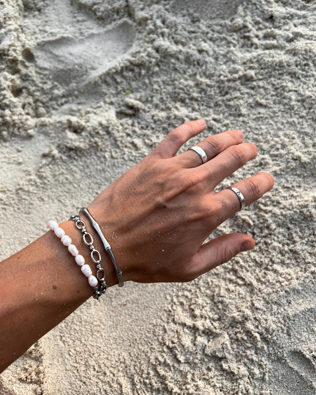 Wrist adorned with stacked silver bracelets including a white bead bracelet and sleek silver bands.