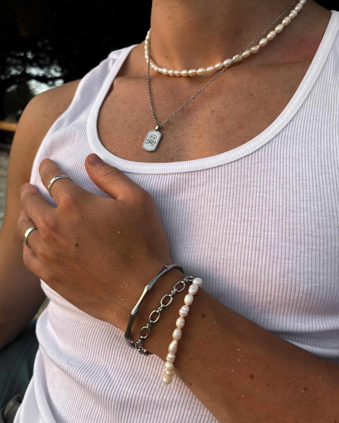 Layered jewelry on the wrist and neck including a pearl bracelet a silver chain with a pendant and a bamboo silver bracelet