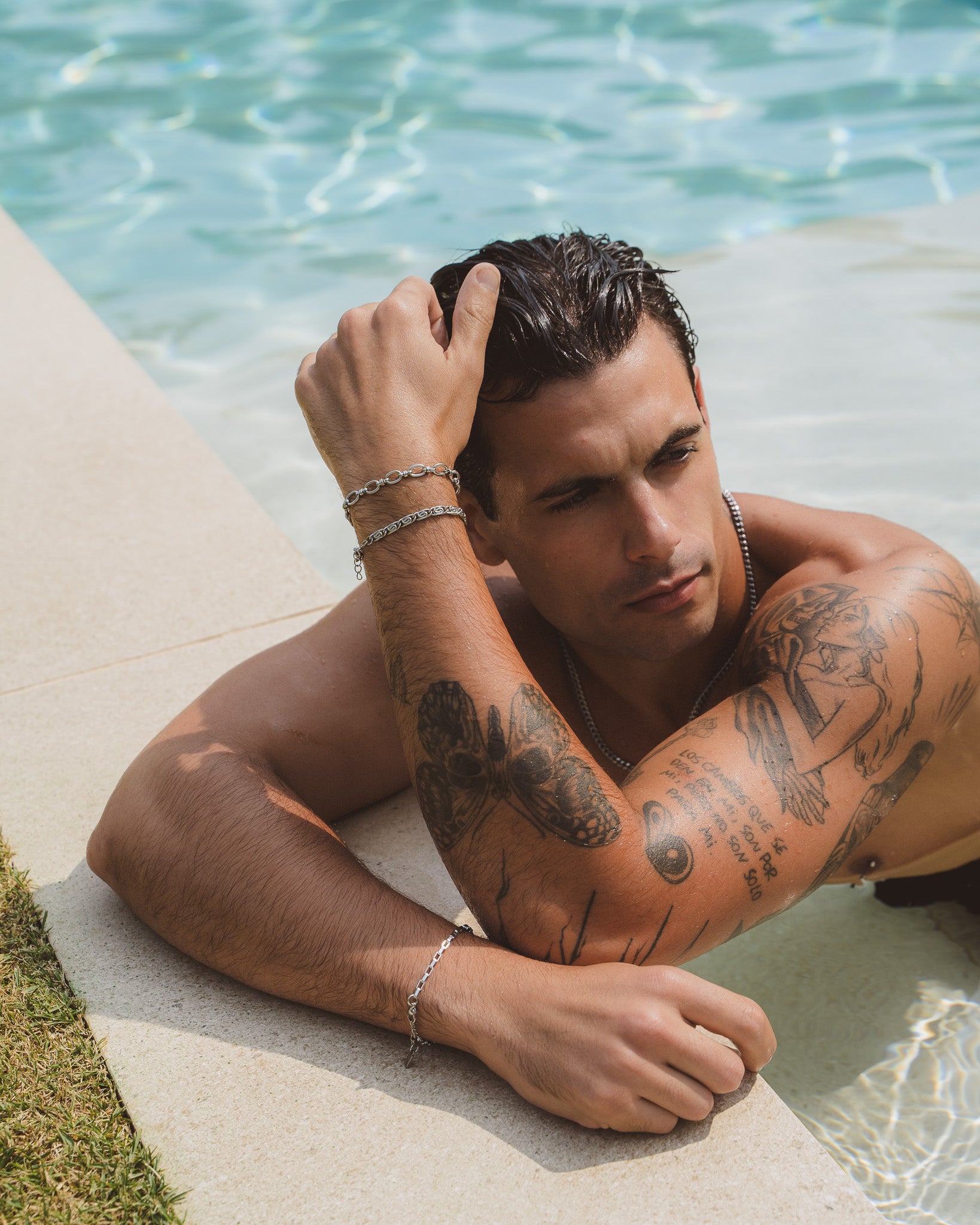 Man wearing stacked silver NUSA bracelets on his wrist beside a pool.