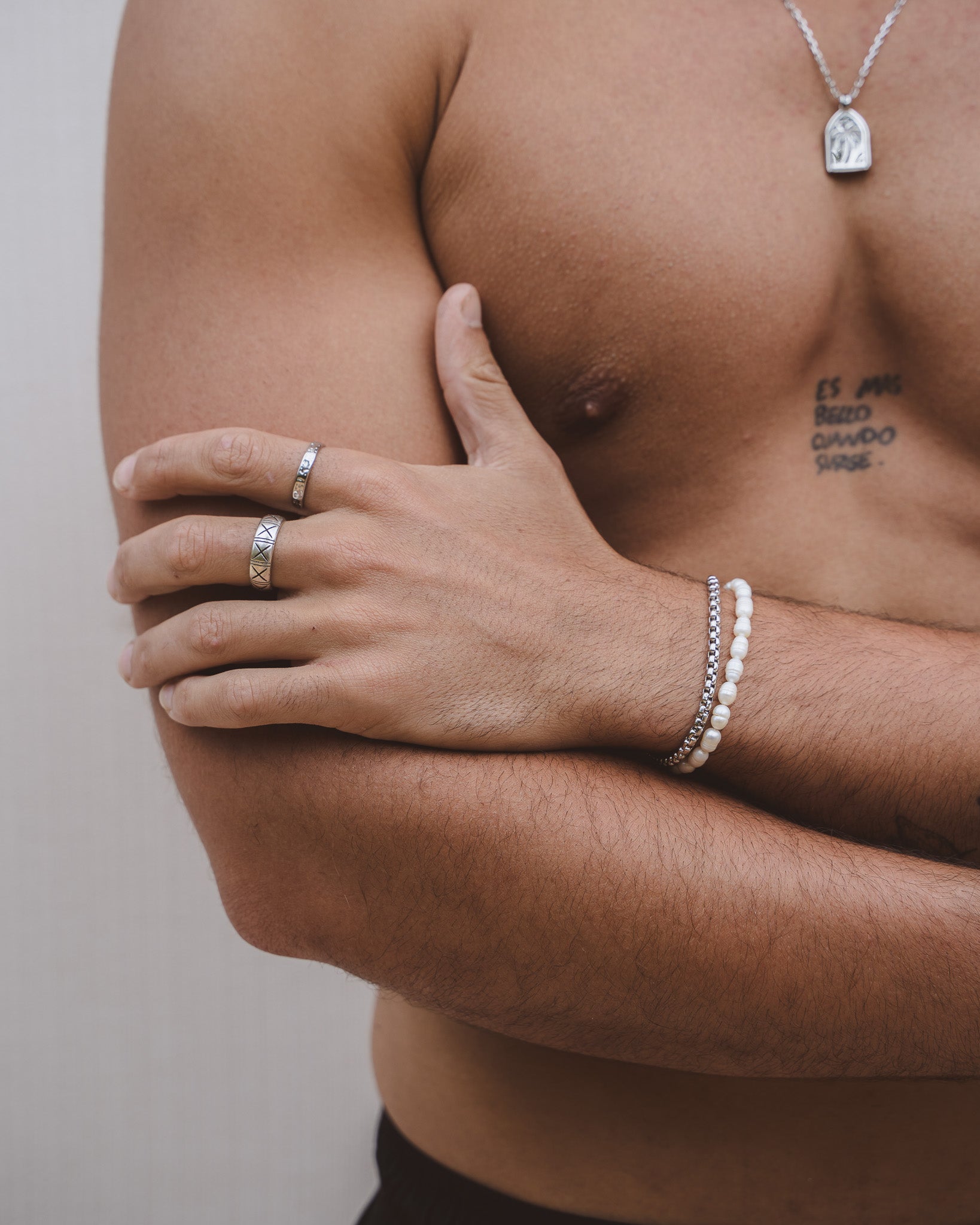 Forearm showing two bracelets a silver linked band and a white beaded bracelet.