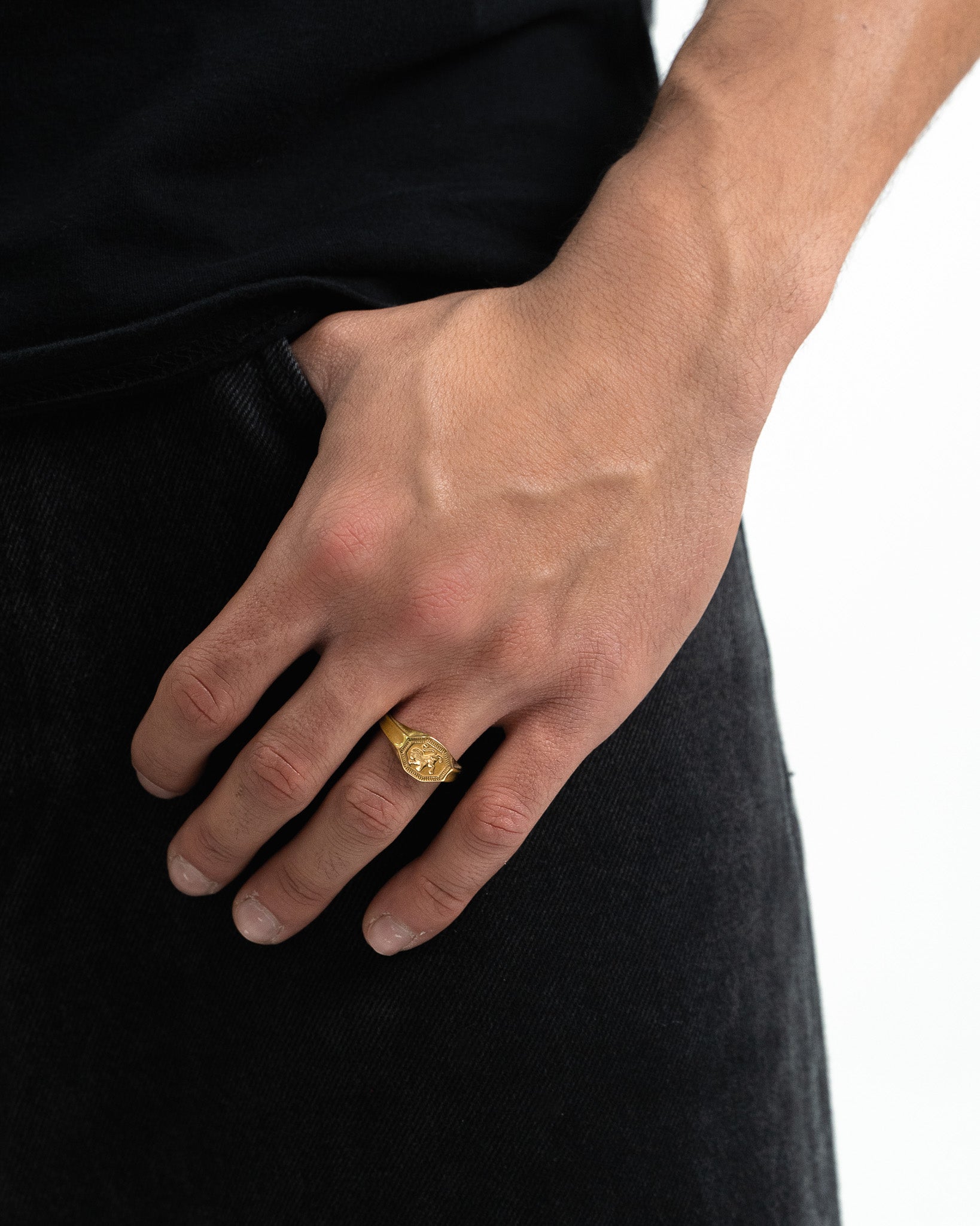 Close up of a gold crest ring on the ring finger of a hand resting on dark fabric