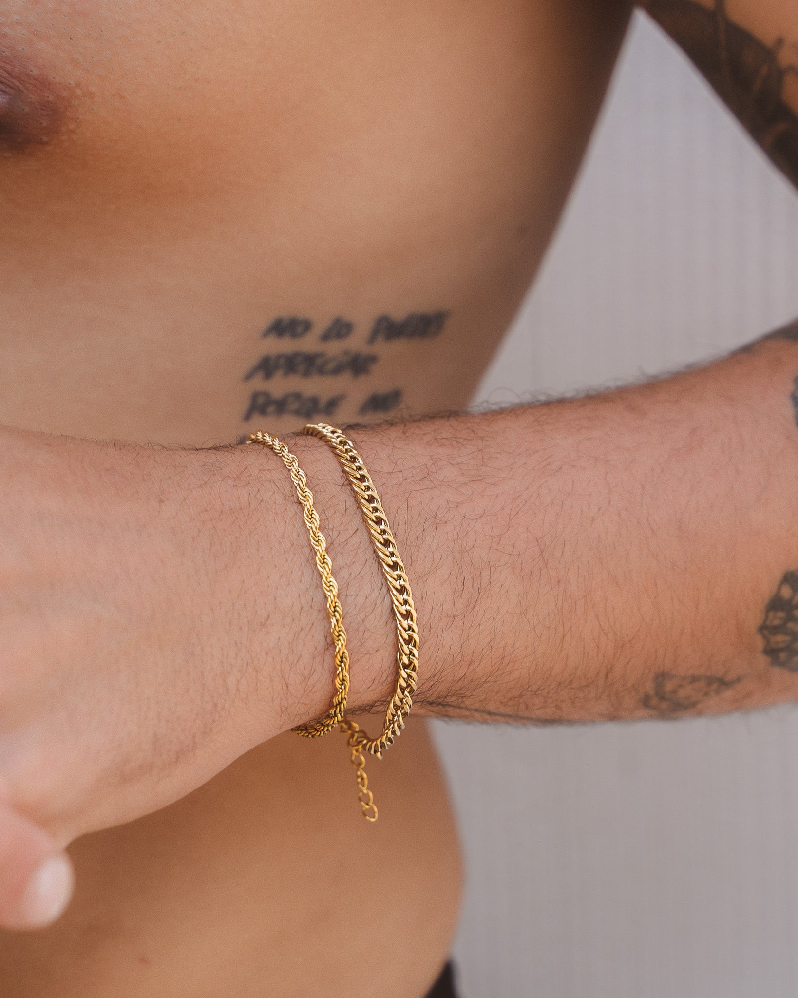 Lazio gold rope chain bracelet on the wrist paired with another bracelet near a tattooed arm by the sea