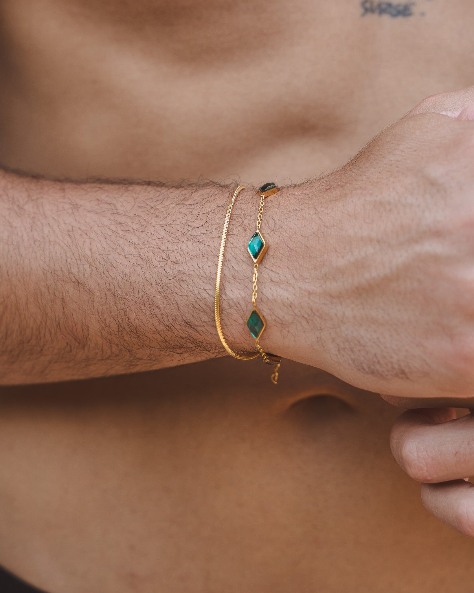 Close up of Lima Gold Bracelets on a wrist showing a slim gold chain and a gemstone accented chain with teal stones