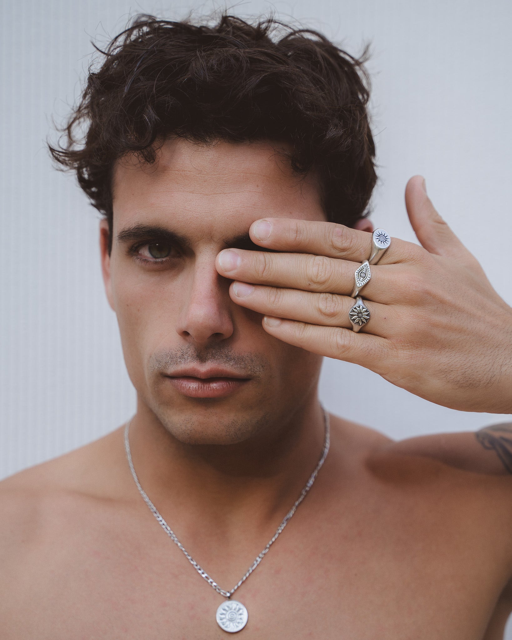 Close up of a man wearing multiple silver rings with sun and eye symbols on his fingers