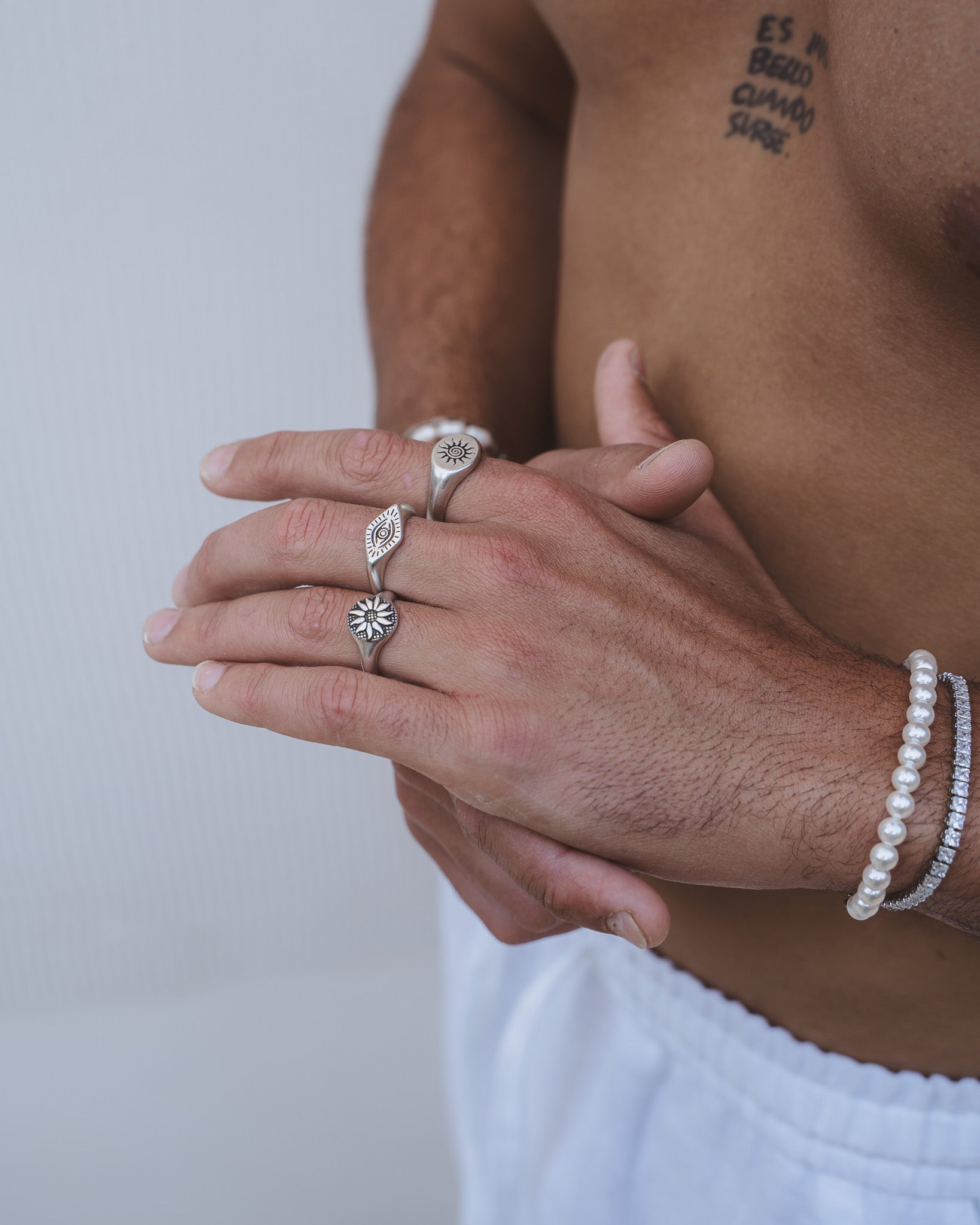Model's hand wearing Fleur Silver Ring with sun motif among stacked rings and a pearl bracelet
