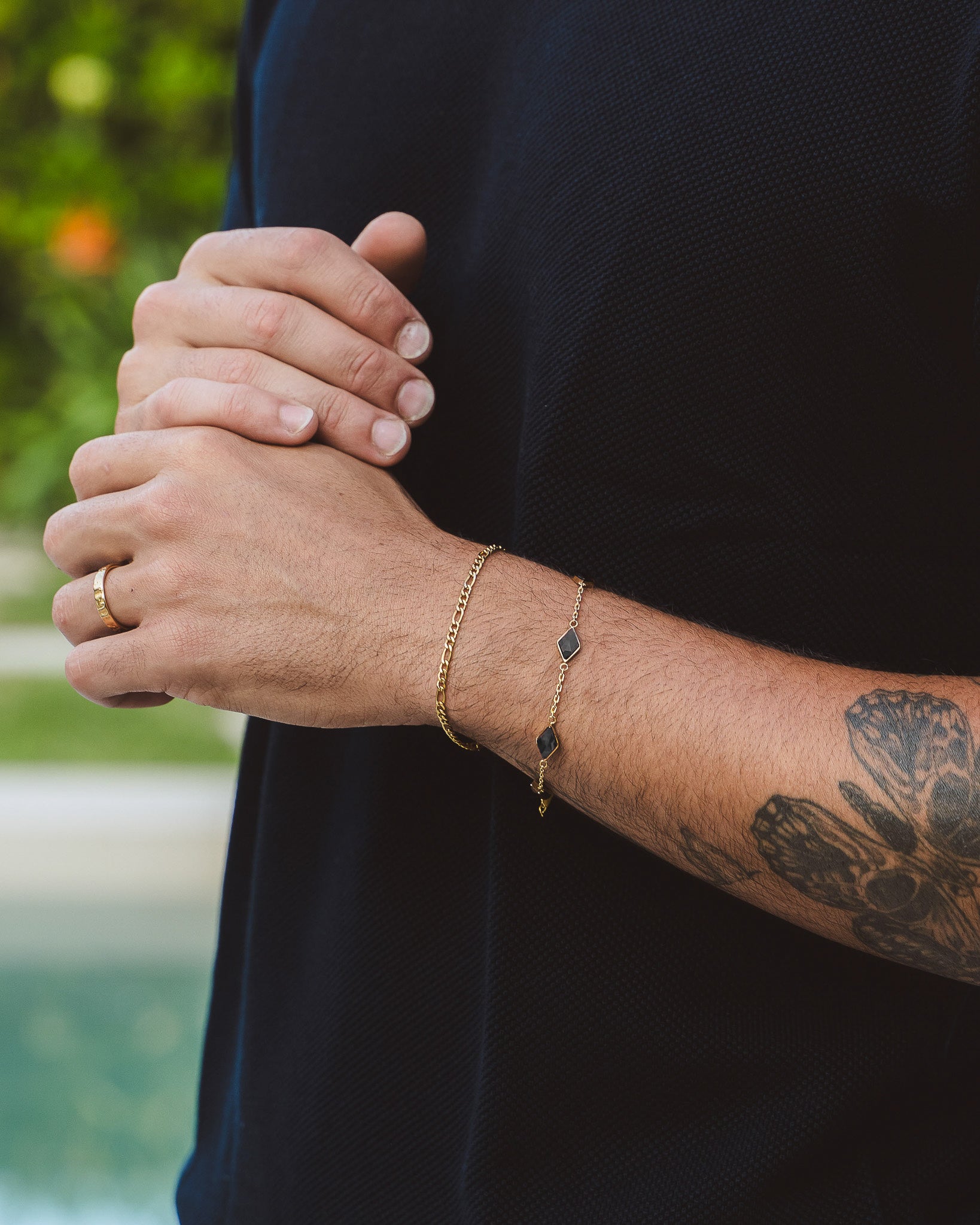 Amberes gold bracelet with square black gemstones on a forearm wearing a dark shirt