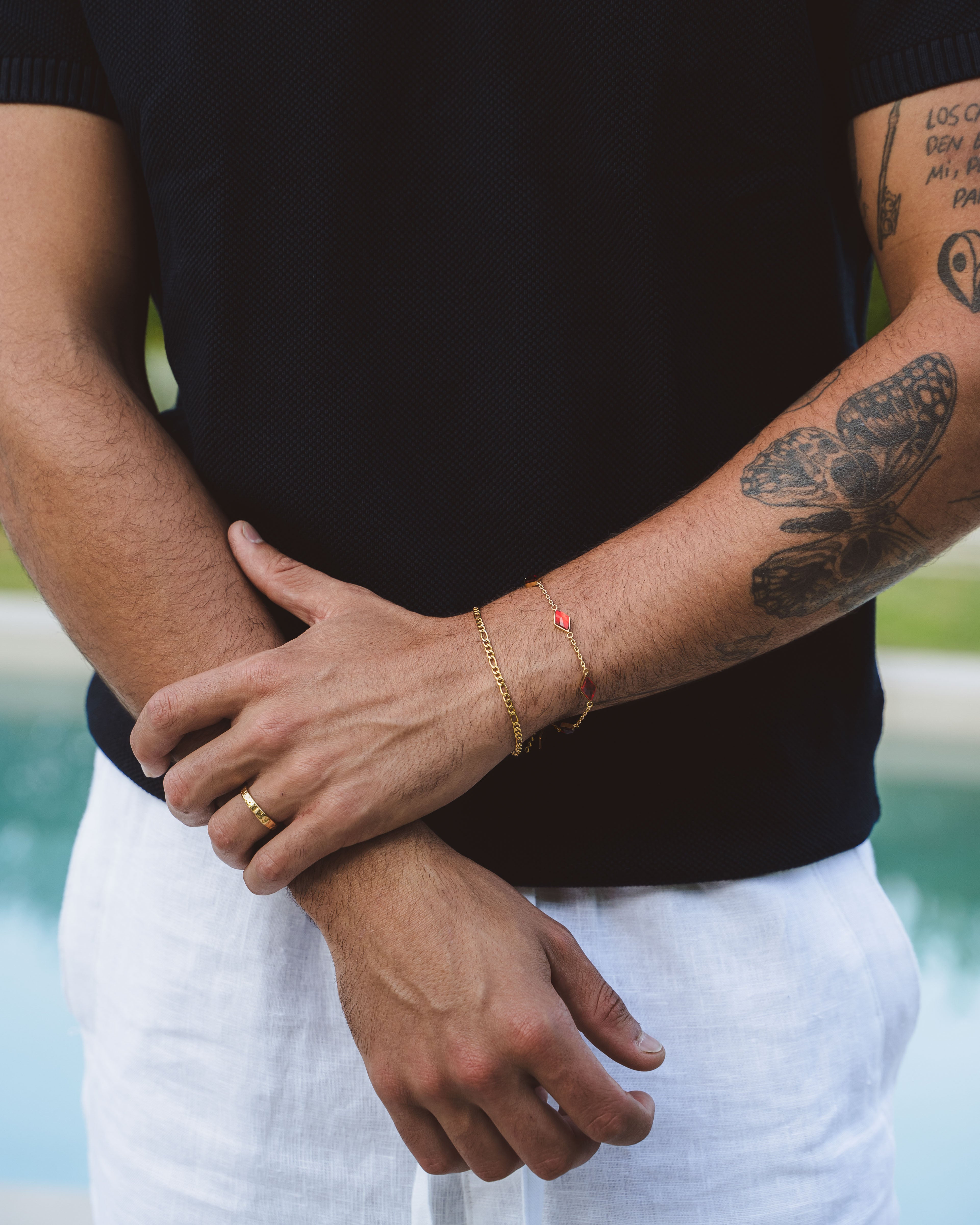 Close-up of Amalfi Gold bracelet with red gemstone charm on a man’s wrist, with visible tattooed forearm