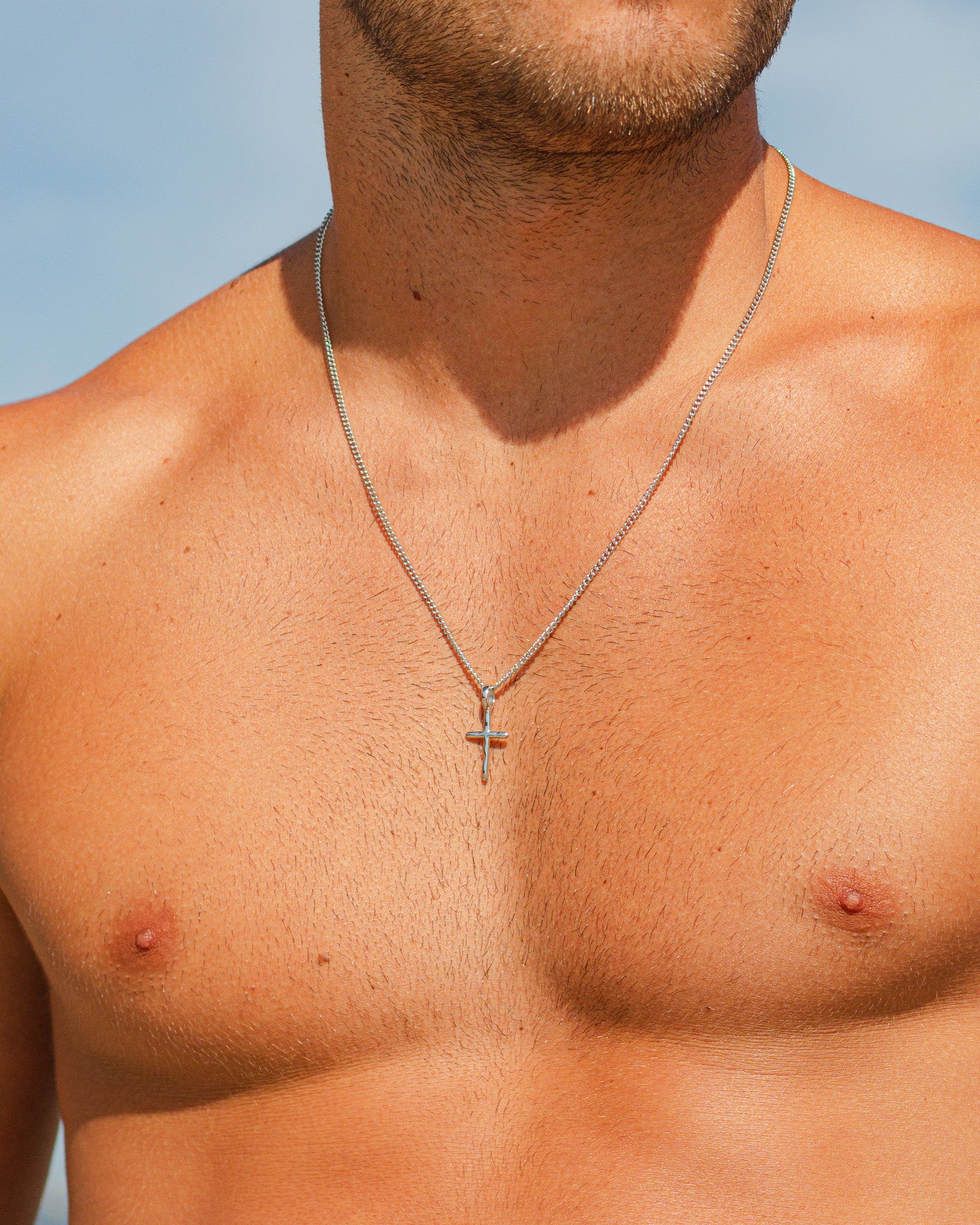 Close up of a silver chain necklace around a man’s neck against a blue sky.