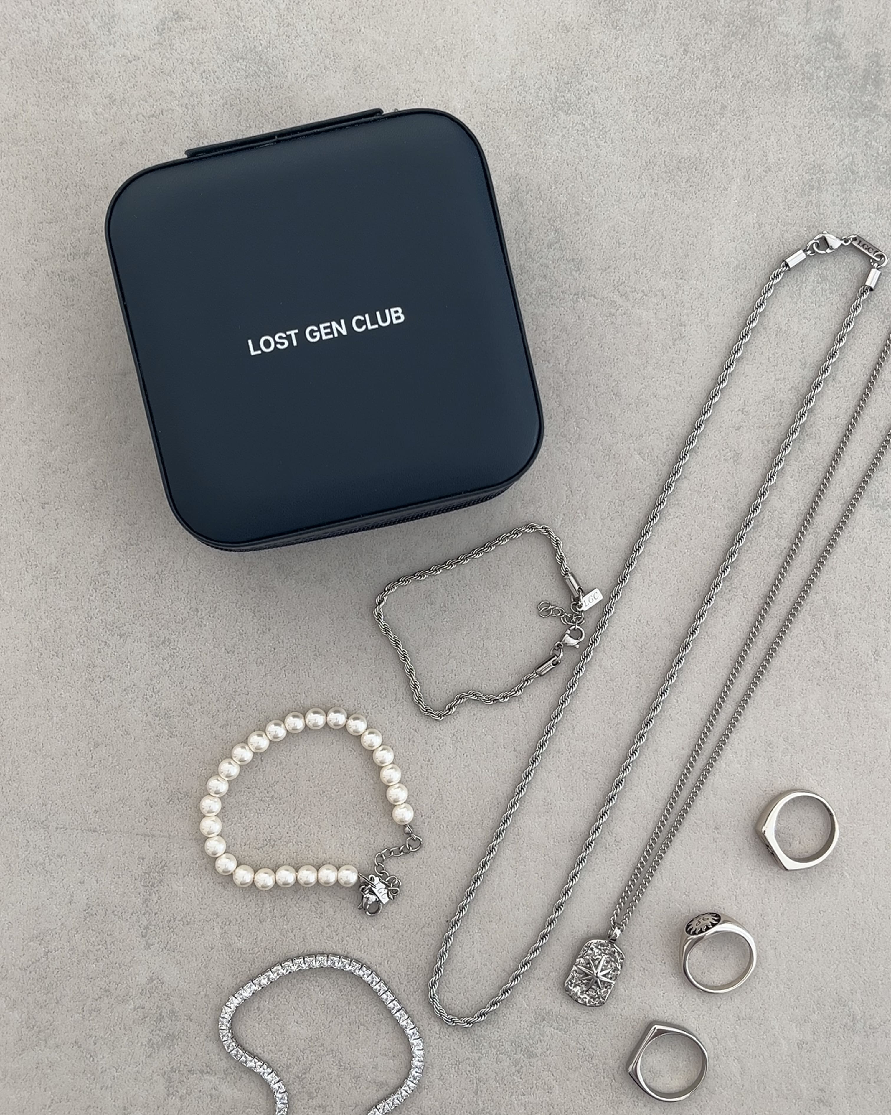 Dark navy square travel jewelry case with Lost Gen Club logo beside silver chains.