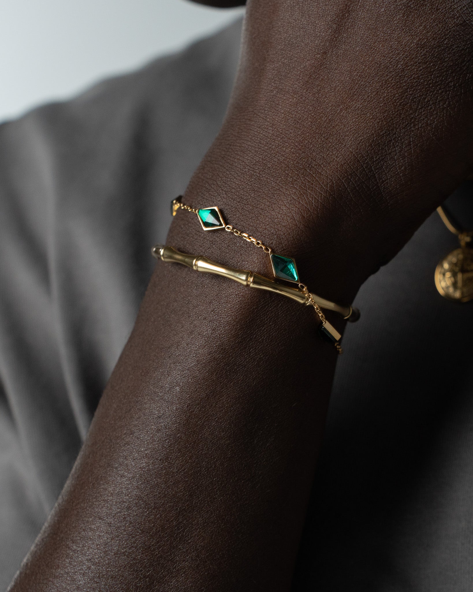 Gold bamboo bracelet with a green diamond shaped gem on a dark skinned wrist