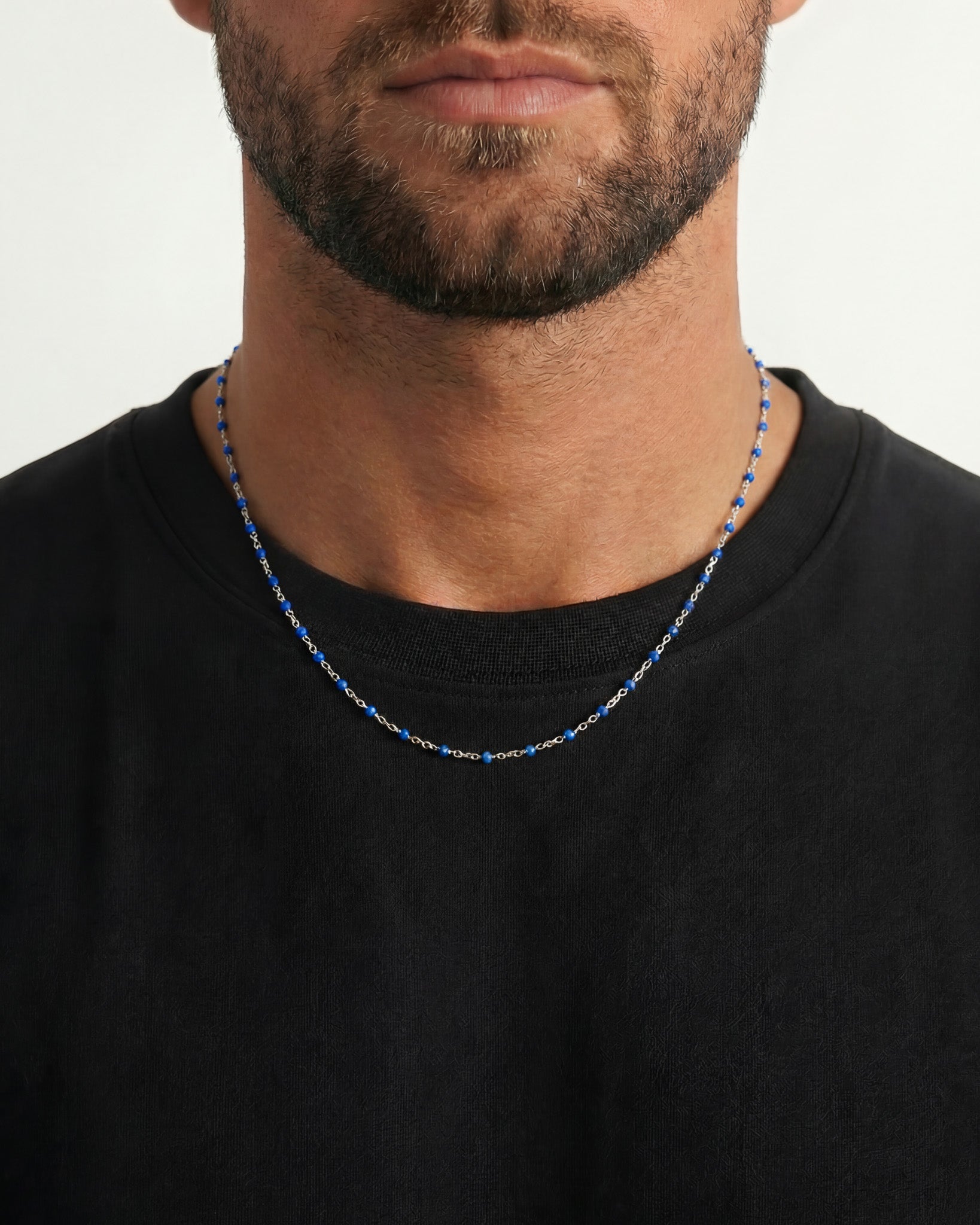 Close up of a silver chain necklace with blue beads resting on a black shirt