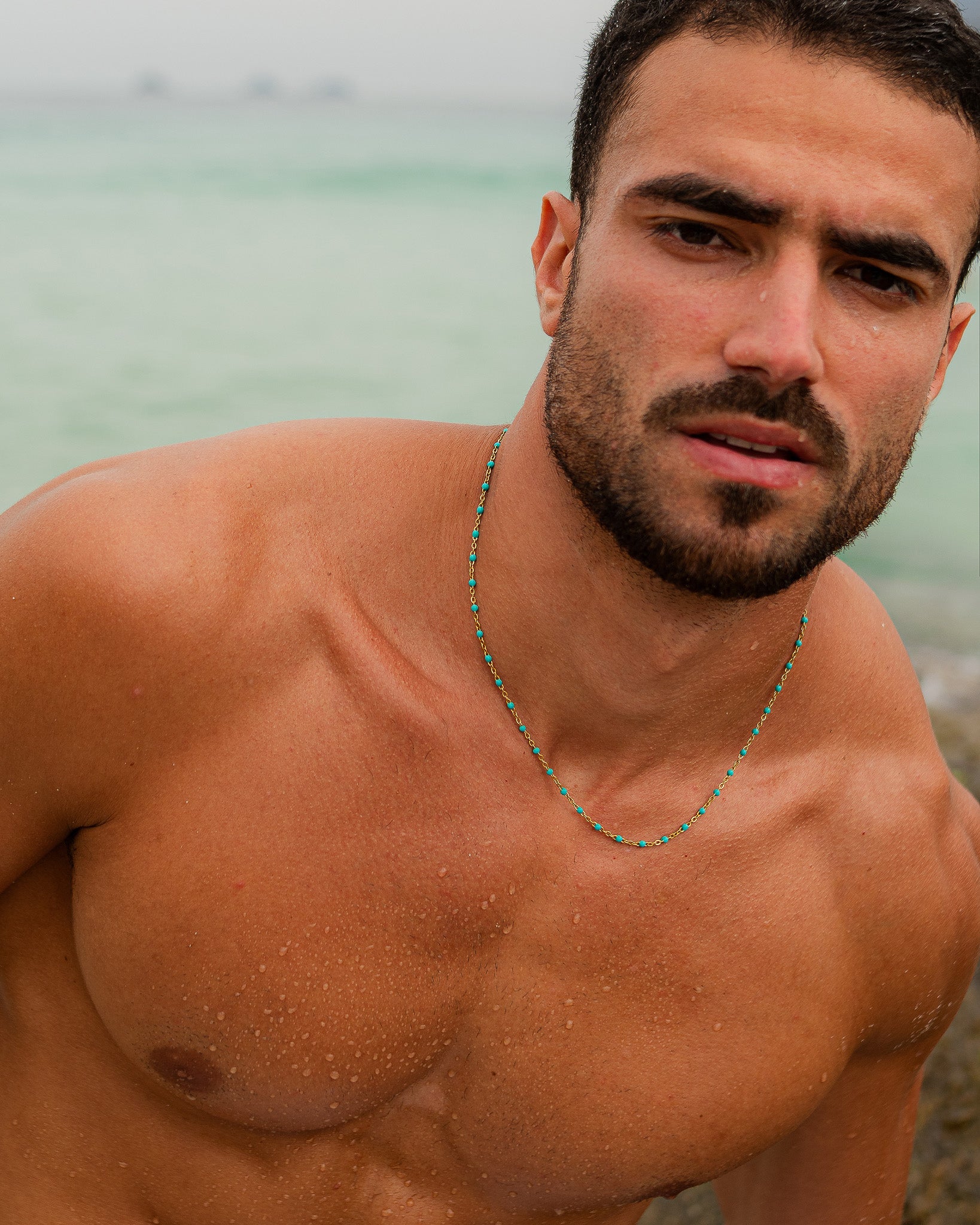 Retrato de un hombre en la playa con una cadena de oro con cuentas turquesa