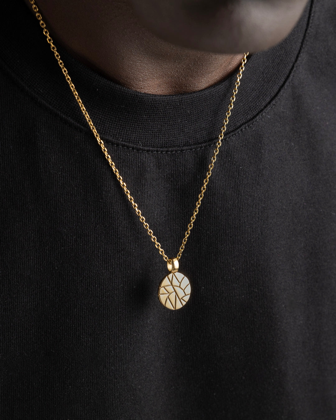 Gold chain with a circular patterned pendant shown close up on black fabric.