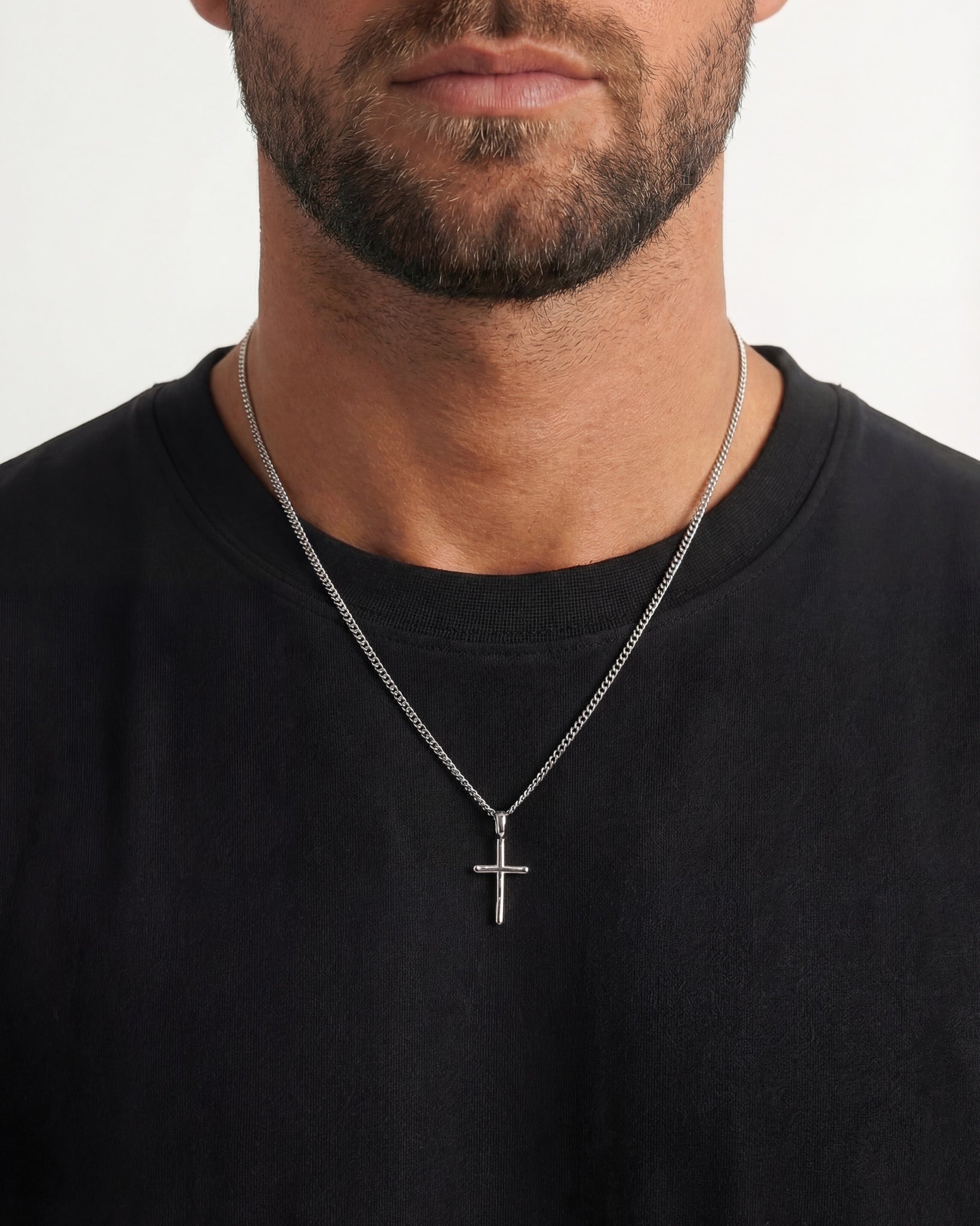 Silver cross pendant on a textured chain around a man's neck