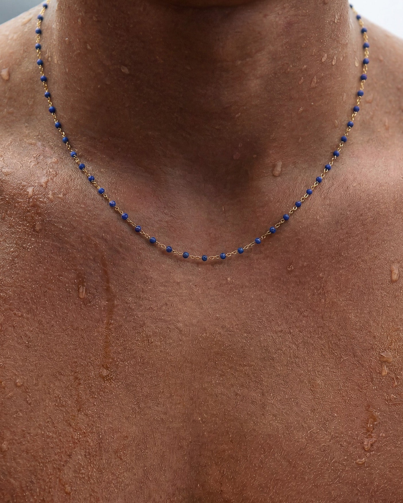 Collar GEM GOLD CHAIN con cuentas azules en cadena dorada sobre el cuello con la piel mojada