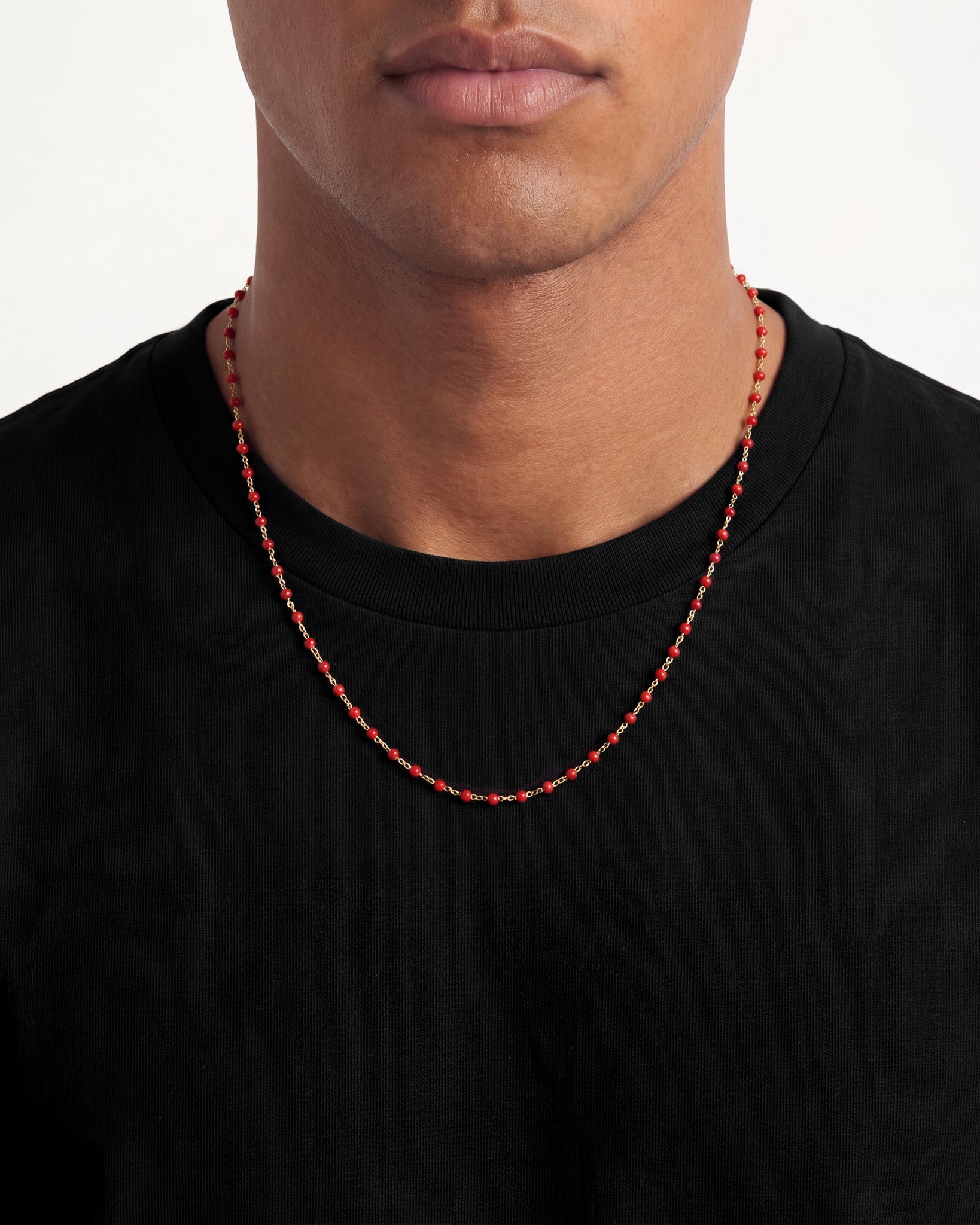 Collar de cadena dorada con cuentas rojas sobre camisa negra