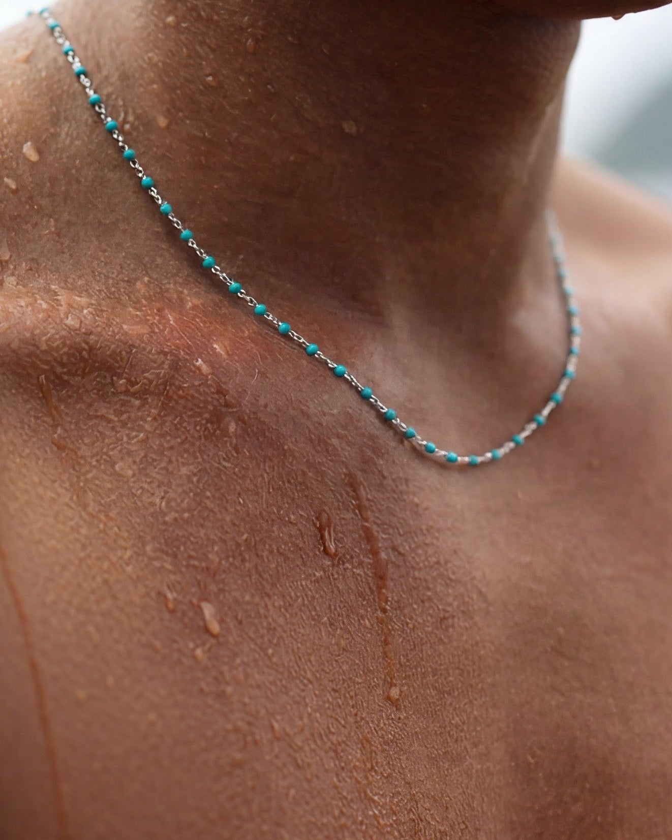Primer plano de cadena plateada con cuentas turquesa sobre un cuello bronceado mojado con gotas de agua