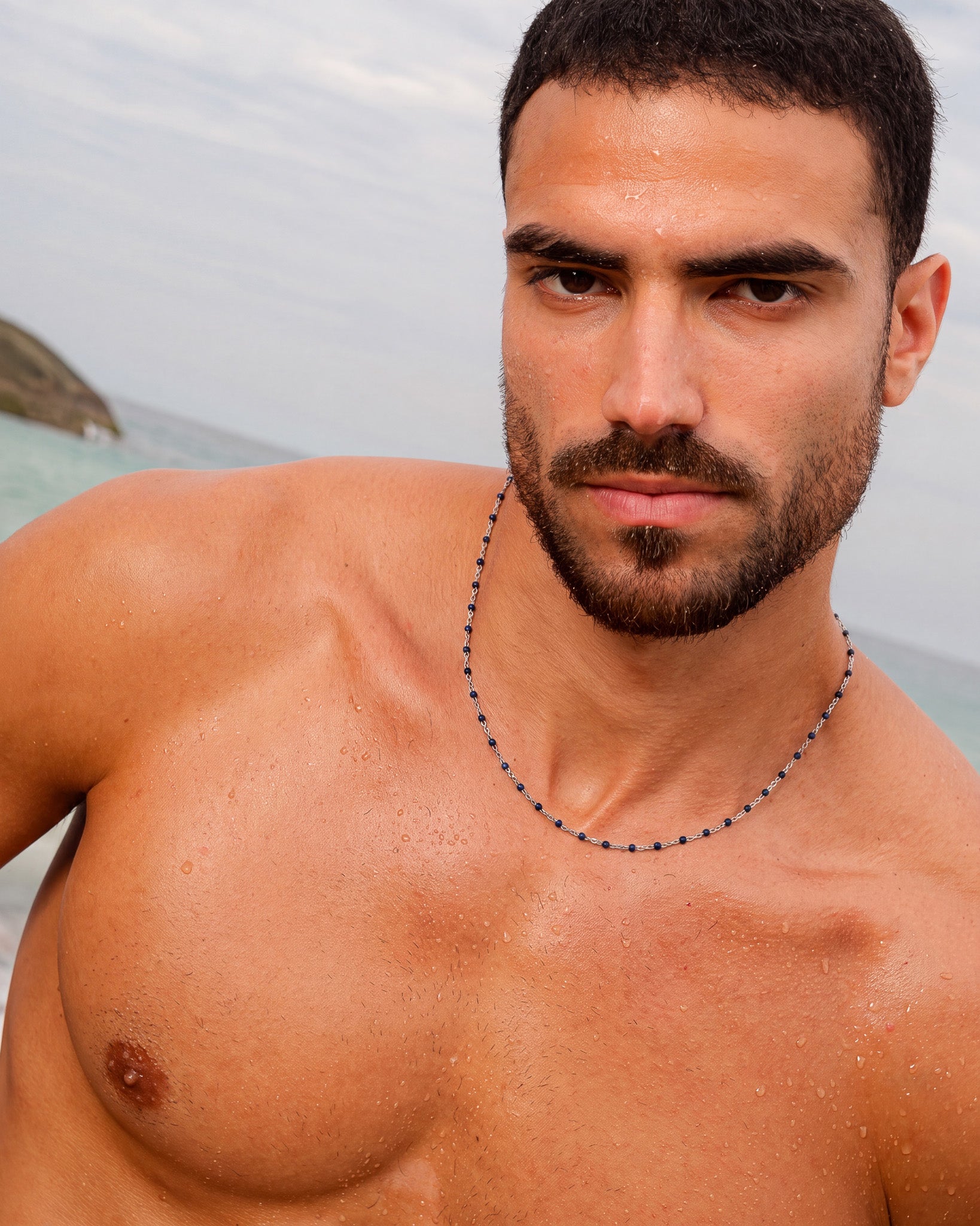 Collar de cadena de plata con cuentas azules en un hombre sin camiseta en la playa.