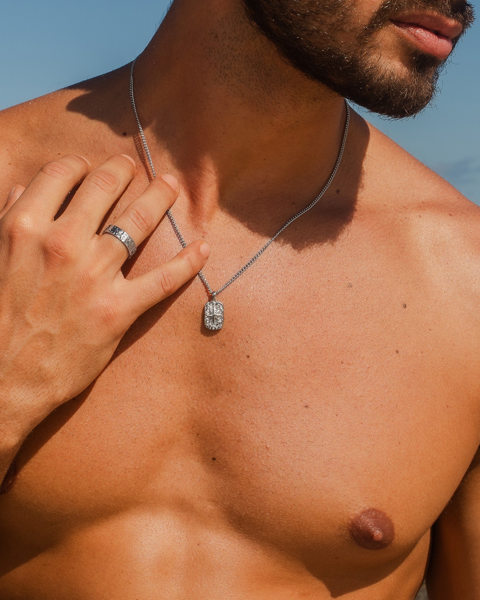 Hombre con collar plateado IBZ con colgante rectangular ornamentado al aire libre.