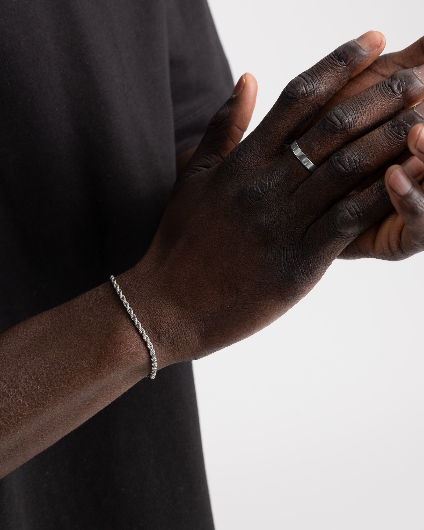 Close up of a dark skinned hand wearing the VERO silver ring on the finger with a silver chain bracelet visible at the wrist