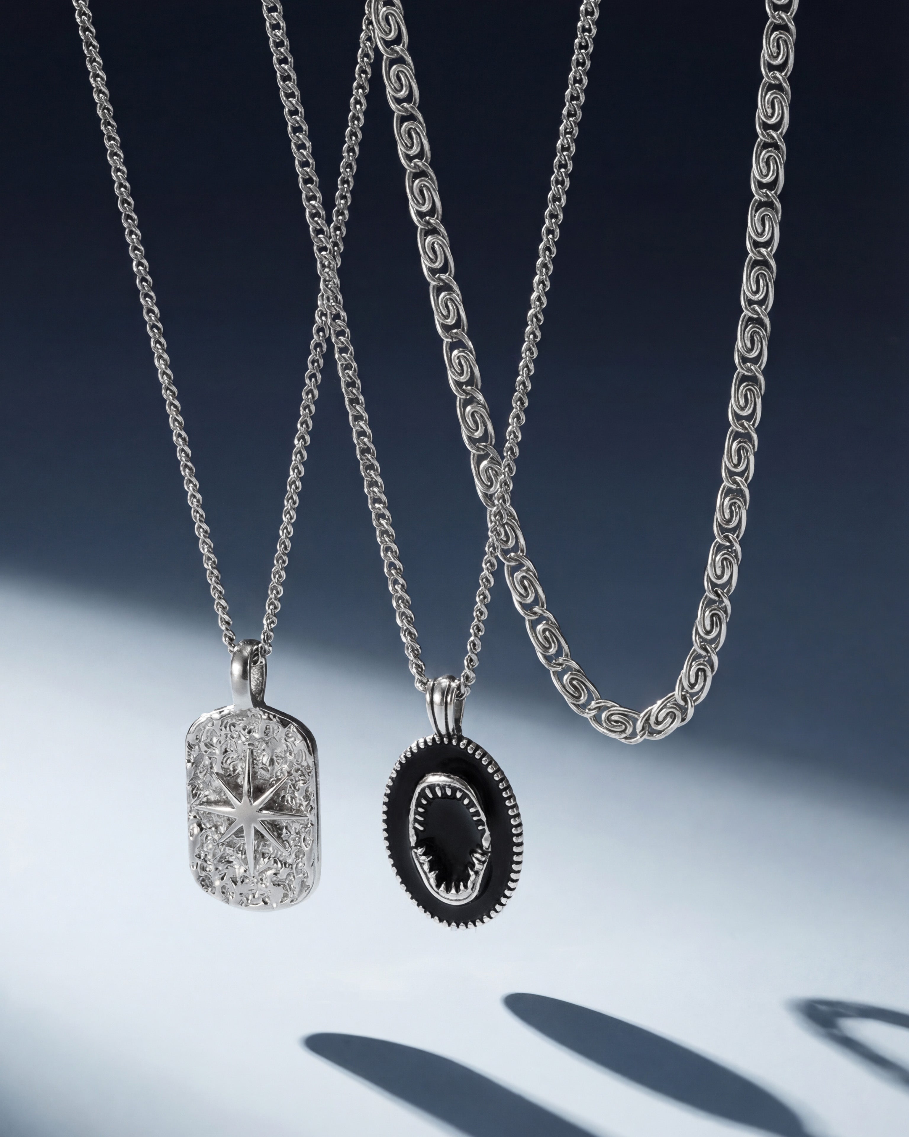 Close up of multiple silver chains with two pendants a silver rectangular one and a black oval pendant