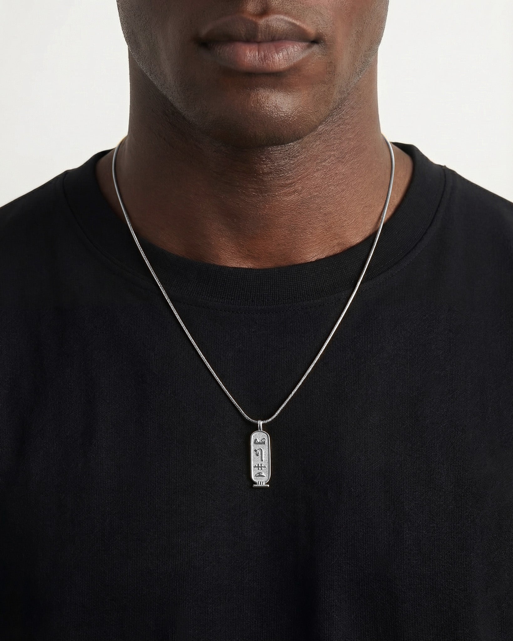 Luxor Silver Necklace pendant with vertical hieroglyphs on a silver chain worn against a black shirt