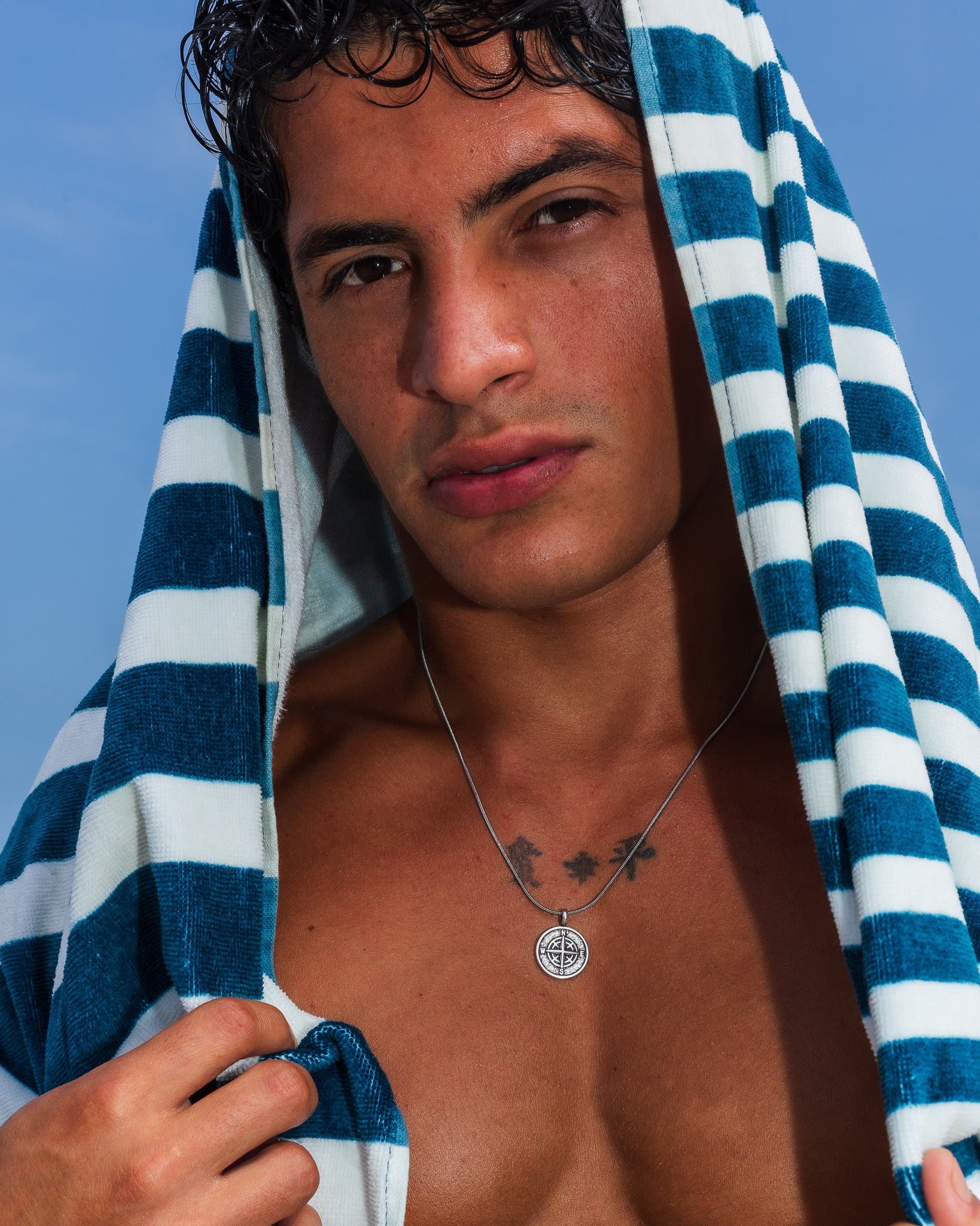 Collar MOJAVE de plata en un hombre con una toalla de rayas azules, con el colgante de brújula a la vista.