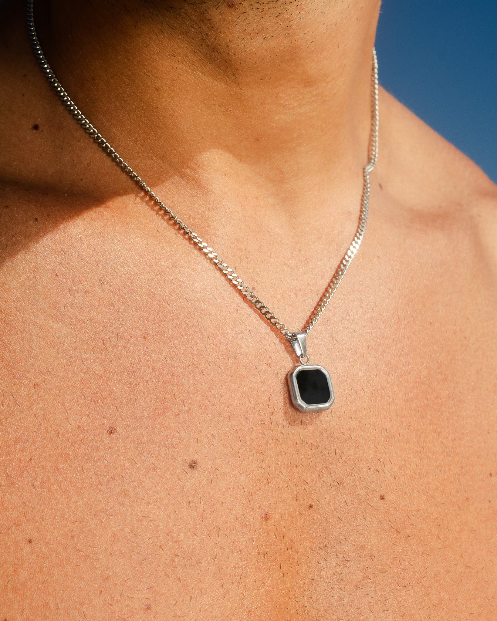 Collar plateado Nova sobre el cuello con la cadena visible contra un cielo azul despejado