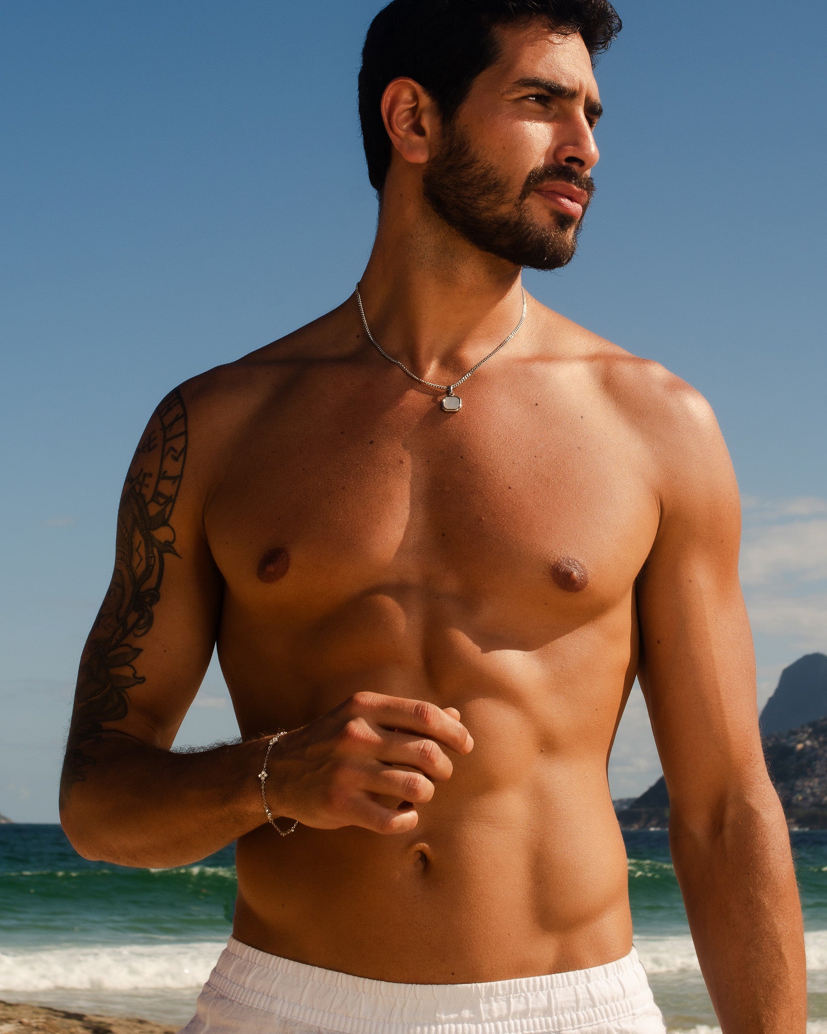 Pulsera plateada Clover en la muñeca izquierda de un hombre sin camiseta en la playa