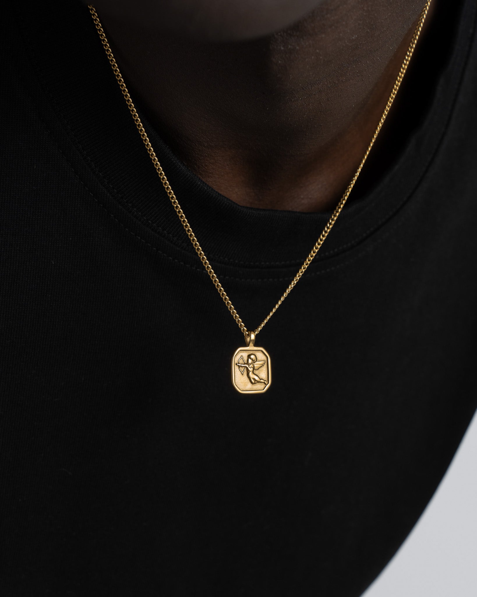 Gold chain necklace with two pendants a round coin and Cupid pendant against dark fabric