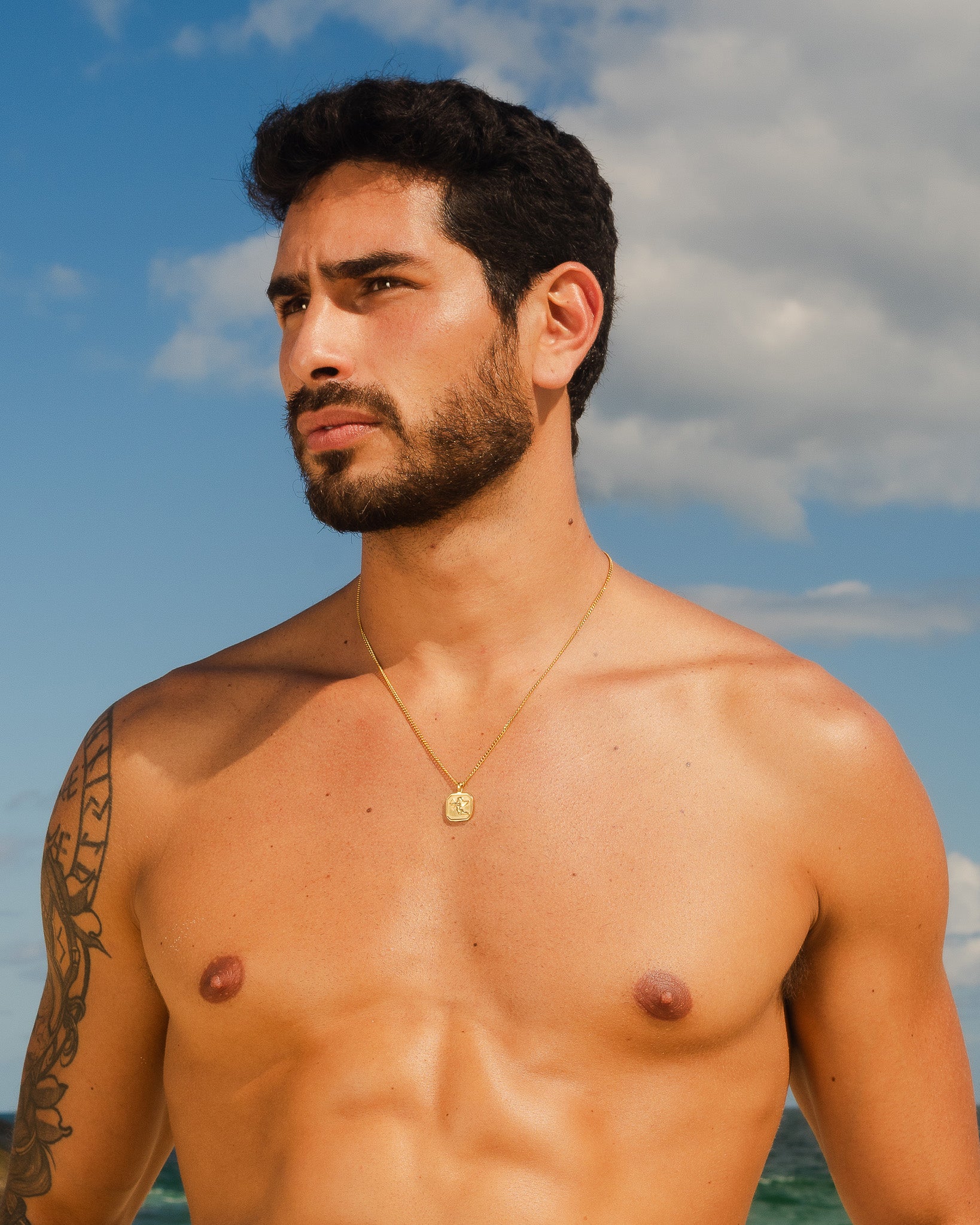 Hombre con collar dorado Savior con colgante cuadrado contra un cielo azul.