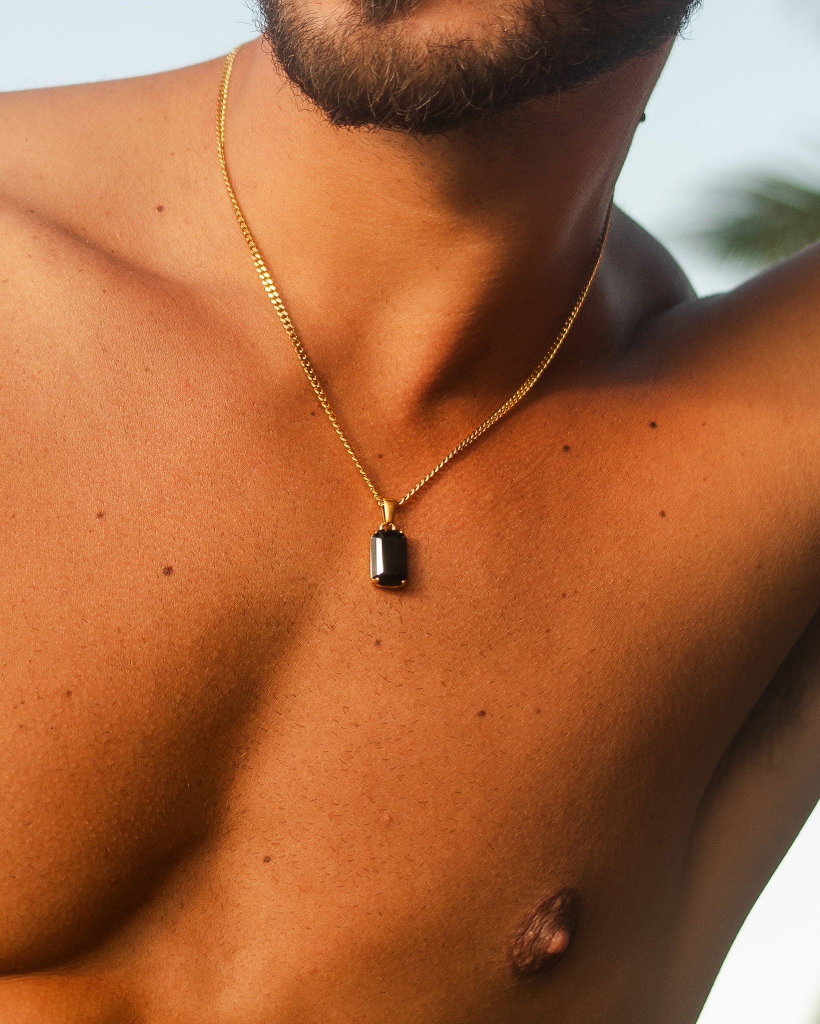 Collar dorado VOLT con pequeño colgante rectangular oscuro sobre el pecho.