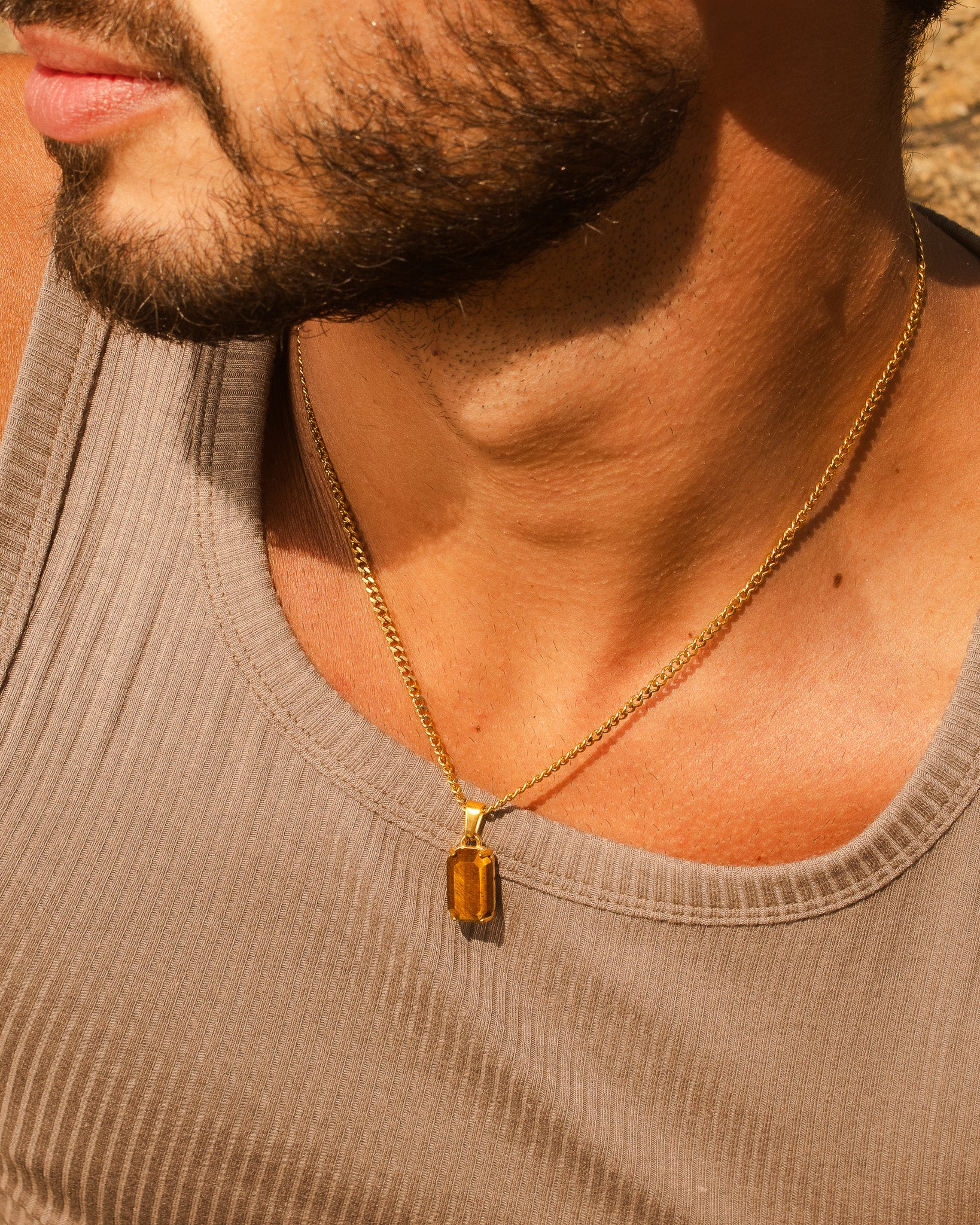 Gold chain necklace with a large rectangular amber pendant on a sunlit chest.
