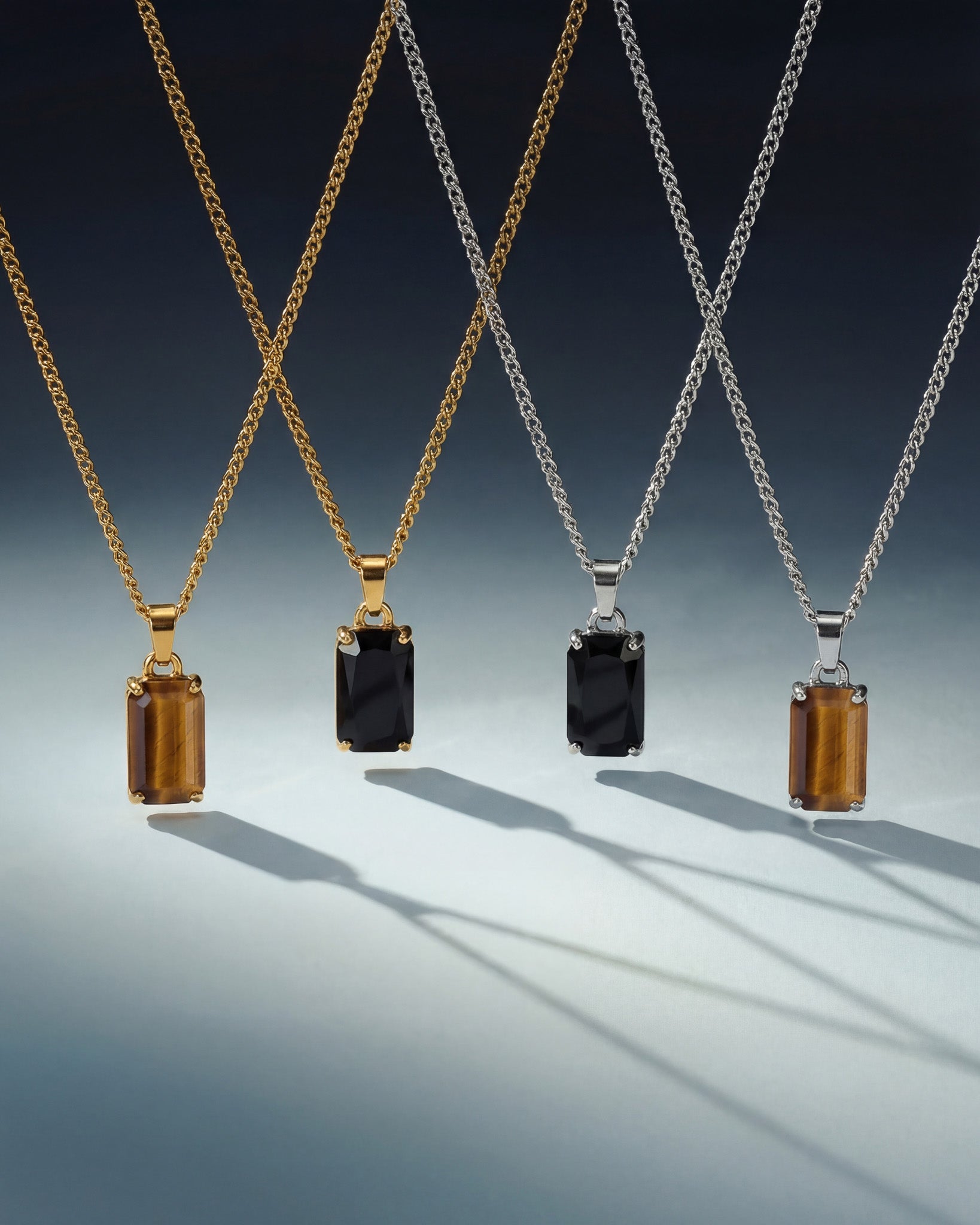 Gold and silver VOLT necklaces with large rectangular tiger's eye pendants against a light gradient background