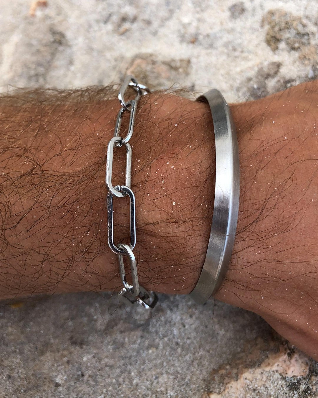 Close up shows two silver bracelets on a wrist a rectangular link chain and a wide smooth cuff