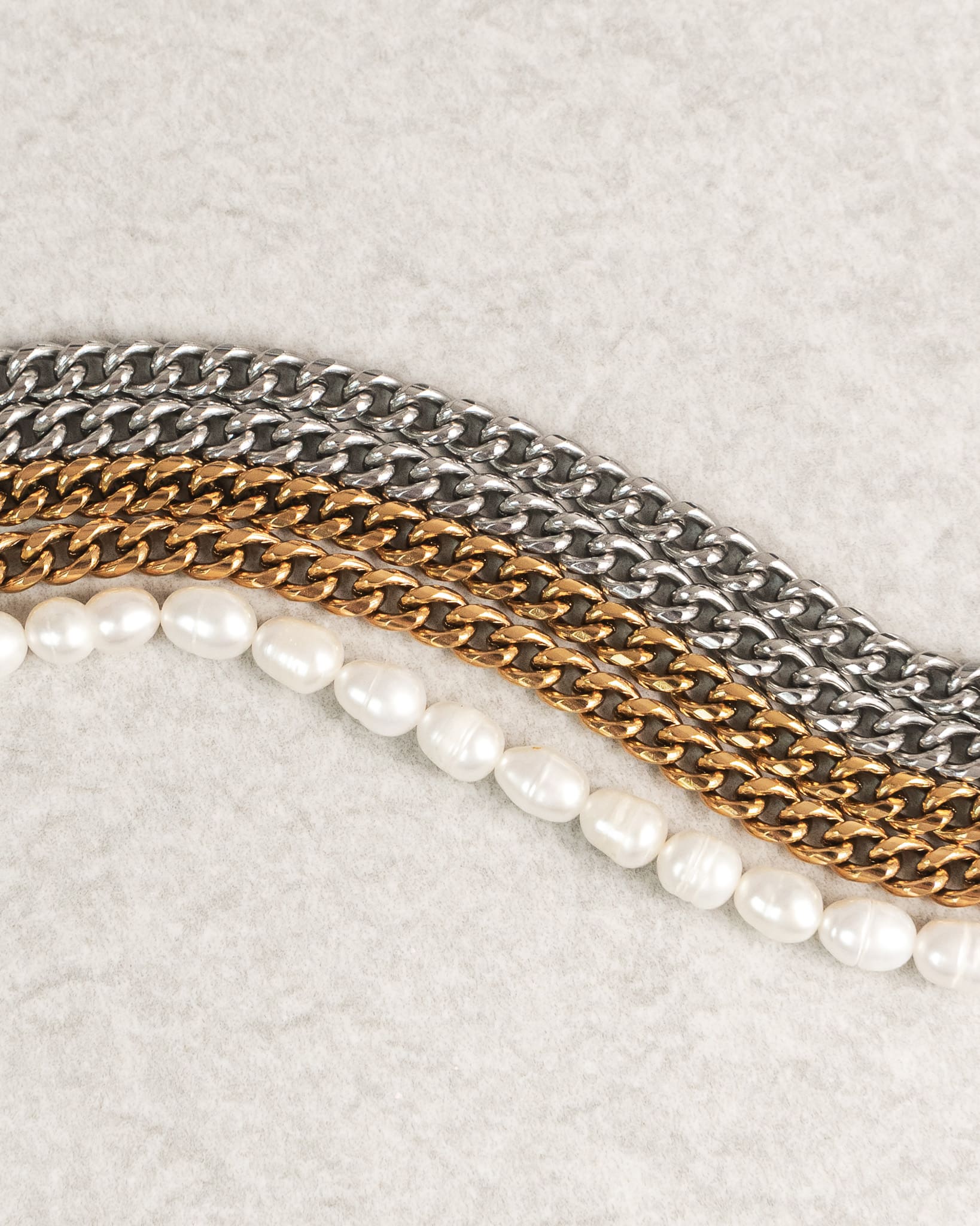 Close-up of layered silver and gold Cuban link chains alongside a freshwater pearl necklace.