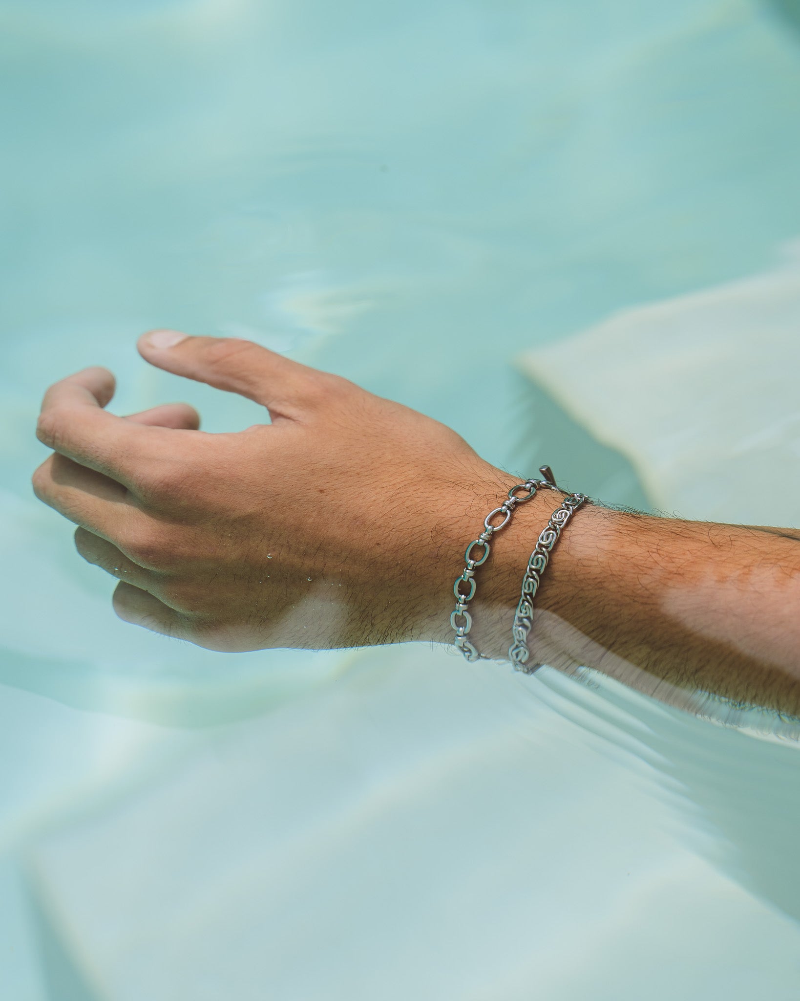 Close-up of a silver bracelet with circular links worn on the wrist against turquoise pool water