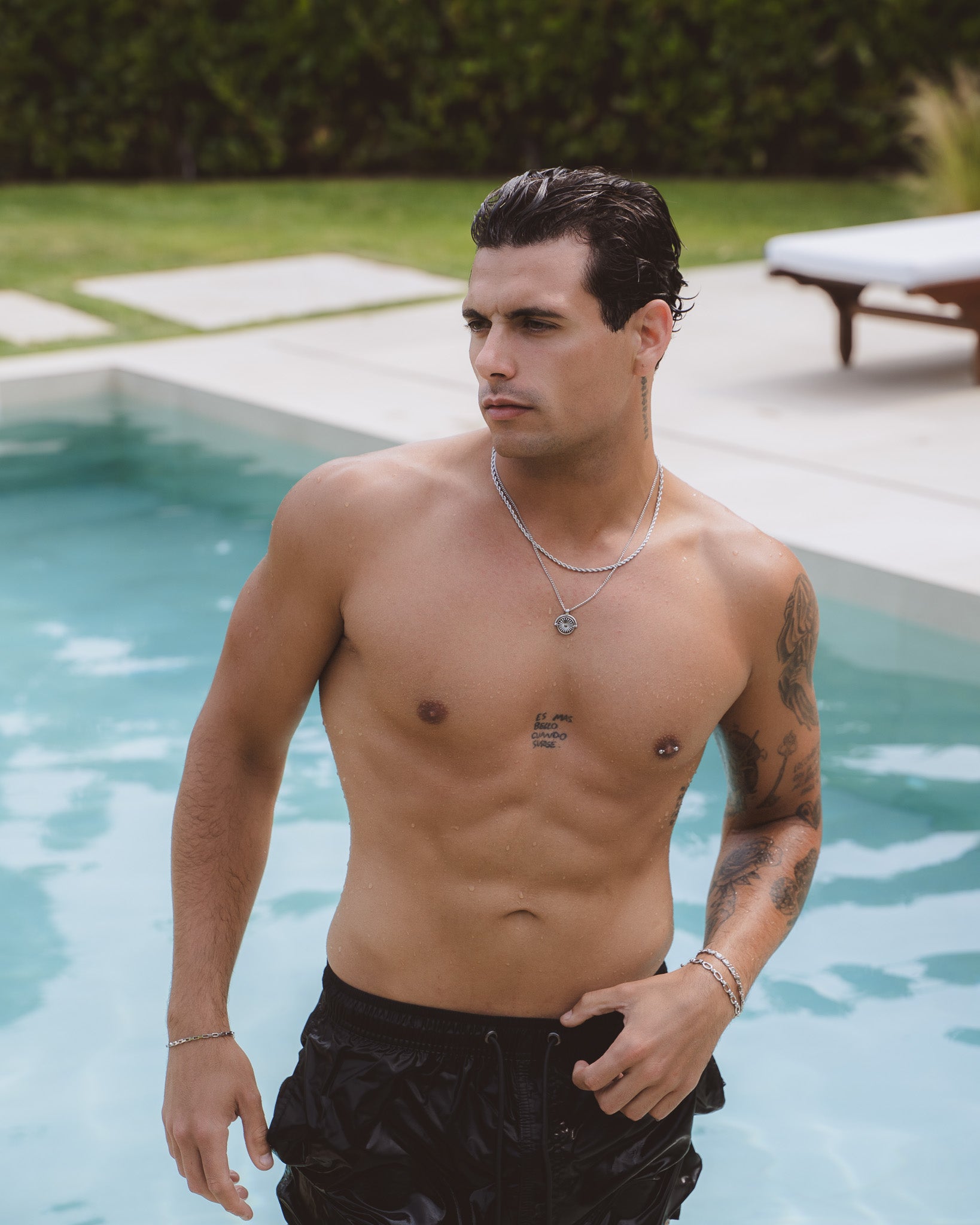 Man by a pool wearing two silver Daisy necklaces with a sunburst pendant.