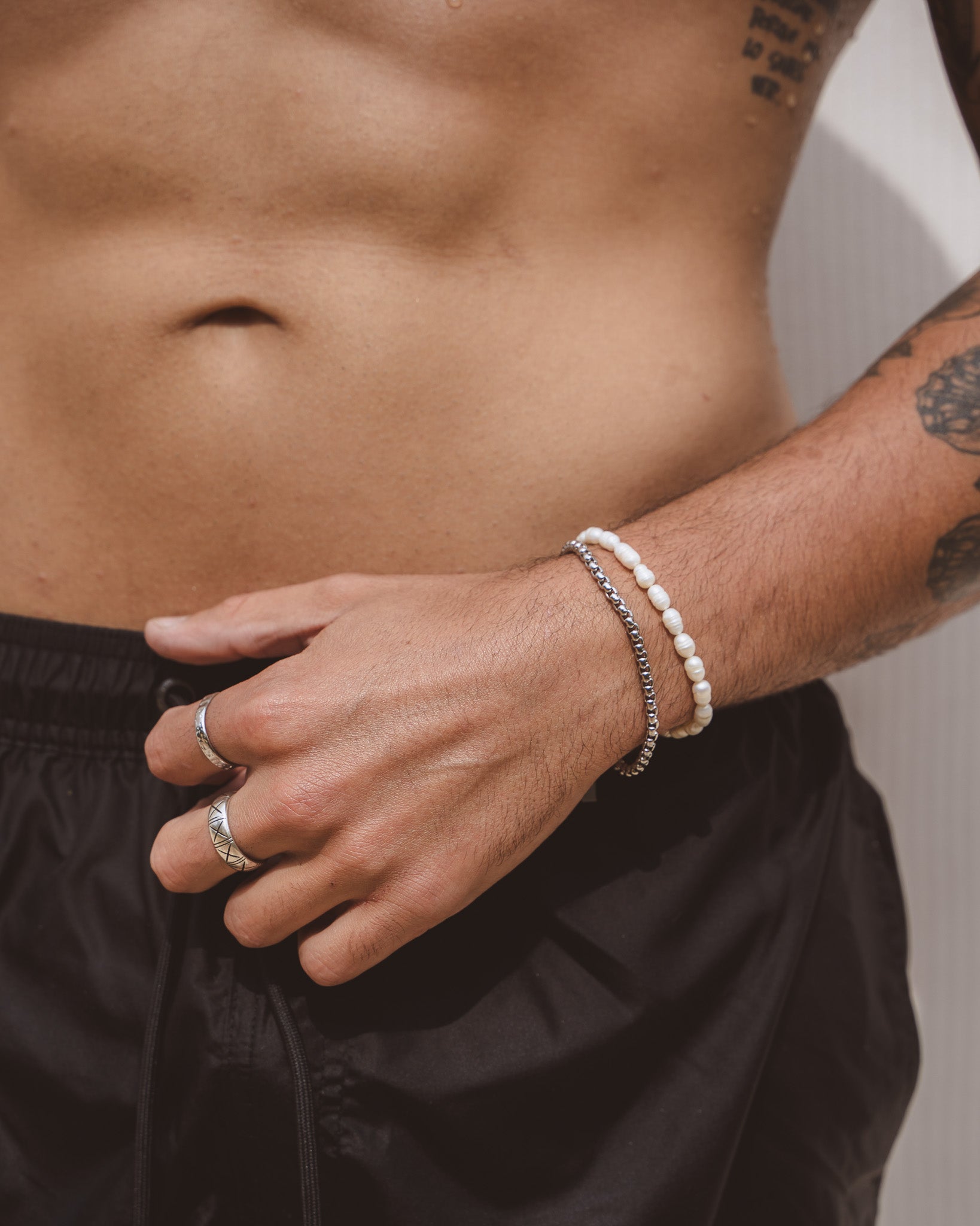 Man wearing NOIR silver bracelet and a white beaded bracelet on the wrist