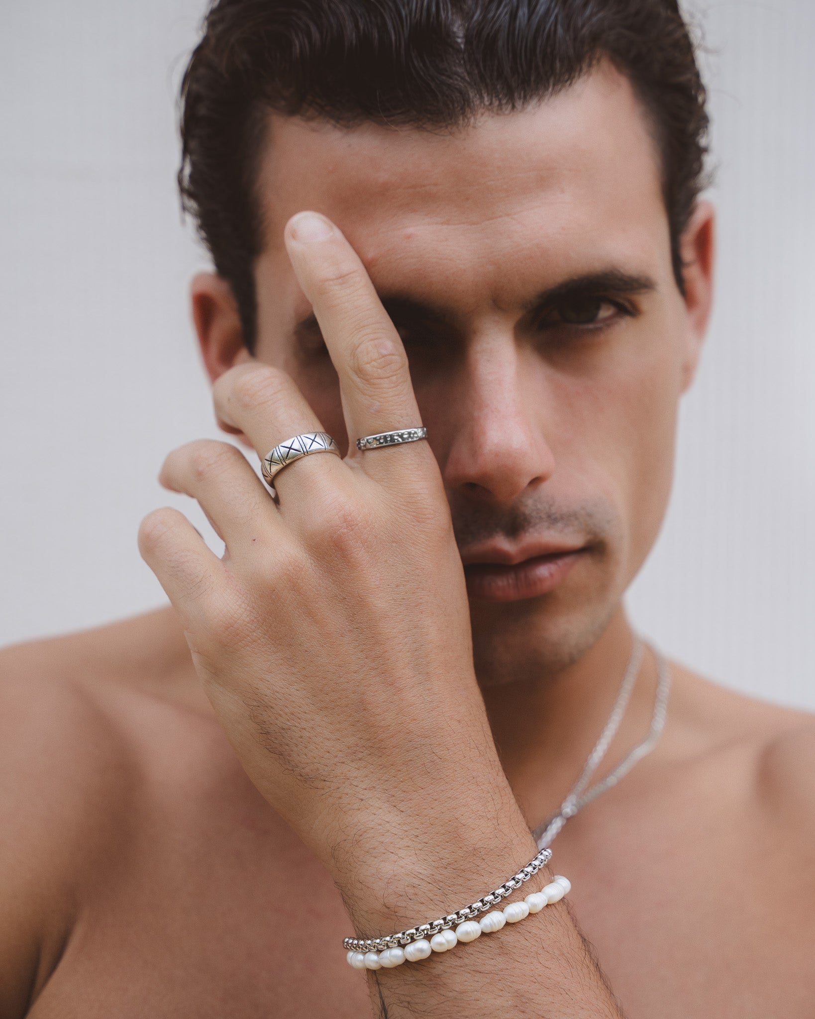 Crisscross patterned silver ring on a finger with a second simple band nearby