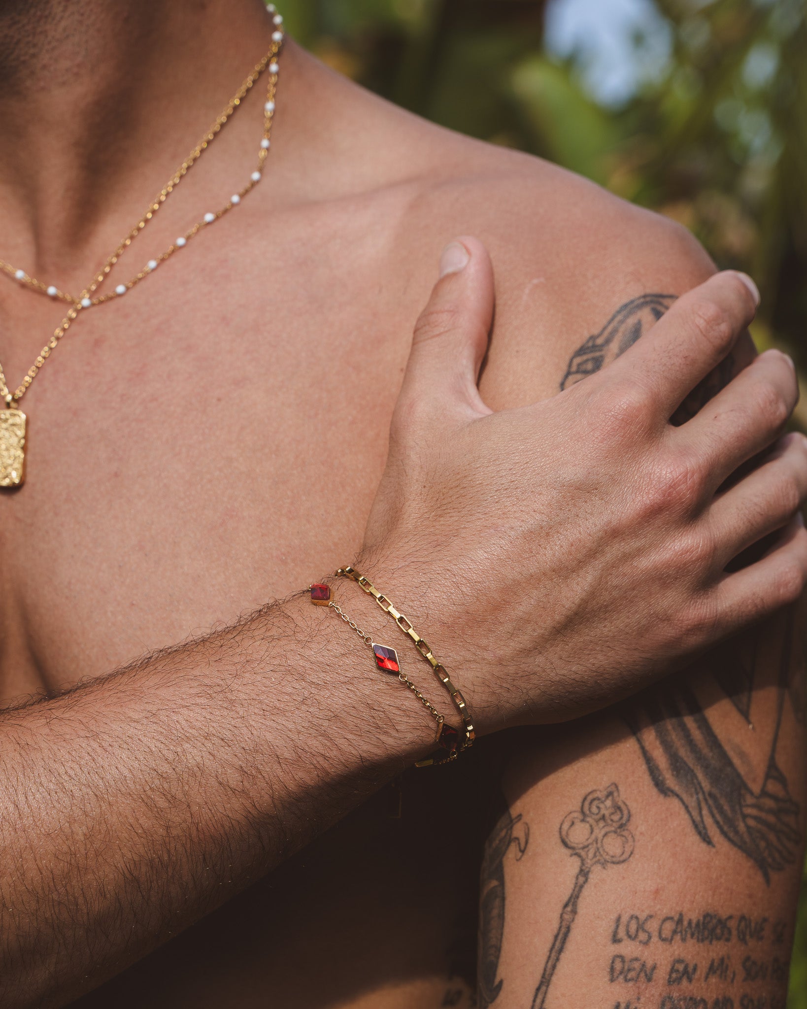 Capri Gold bracelet with rectangular links on a tattooed forearm, paired with a red gemstone bracelet
