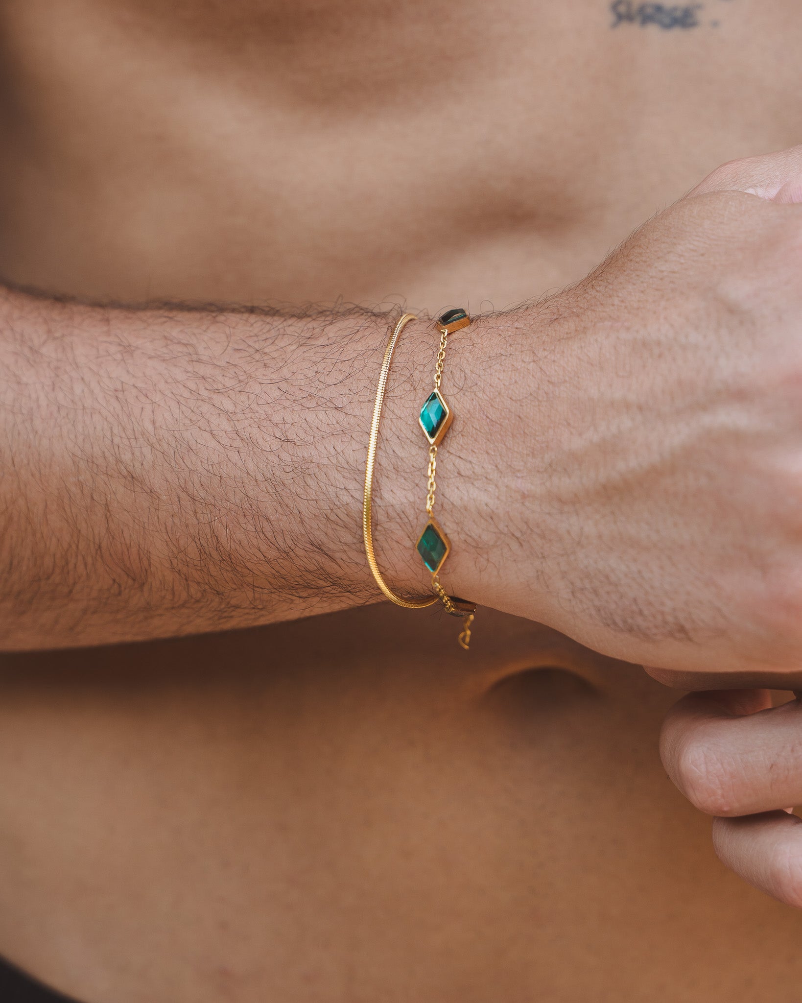Close up of Lima Gold Bracelets on a wrist showing a slim gold chain and a gemstone accented chain with teal stones