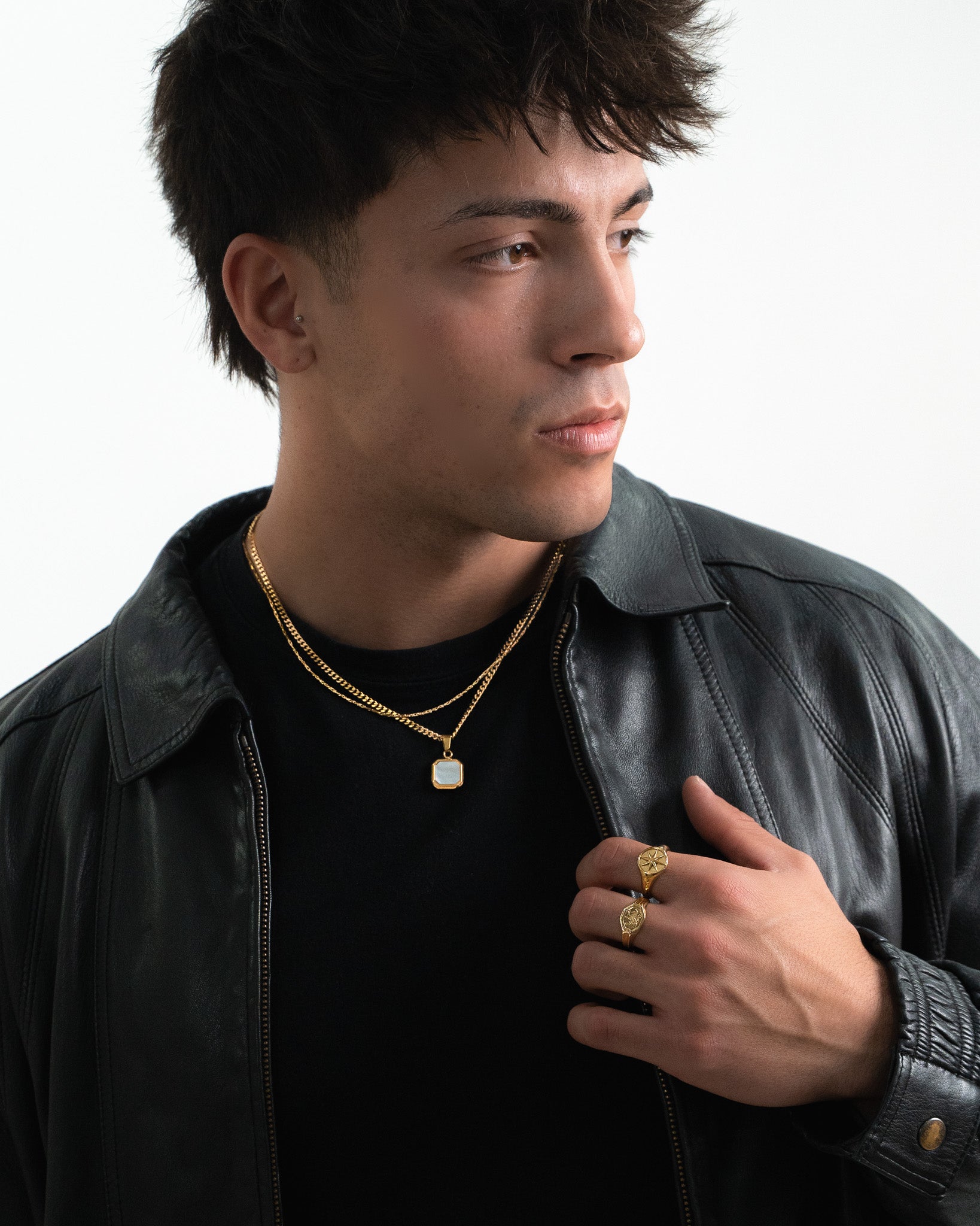 Side profile of a man wearing a NOVA GOLD necklace with a square pale pendant and a black leather jacket