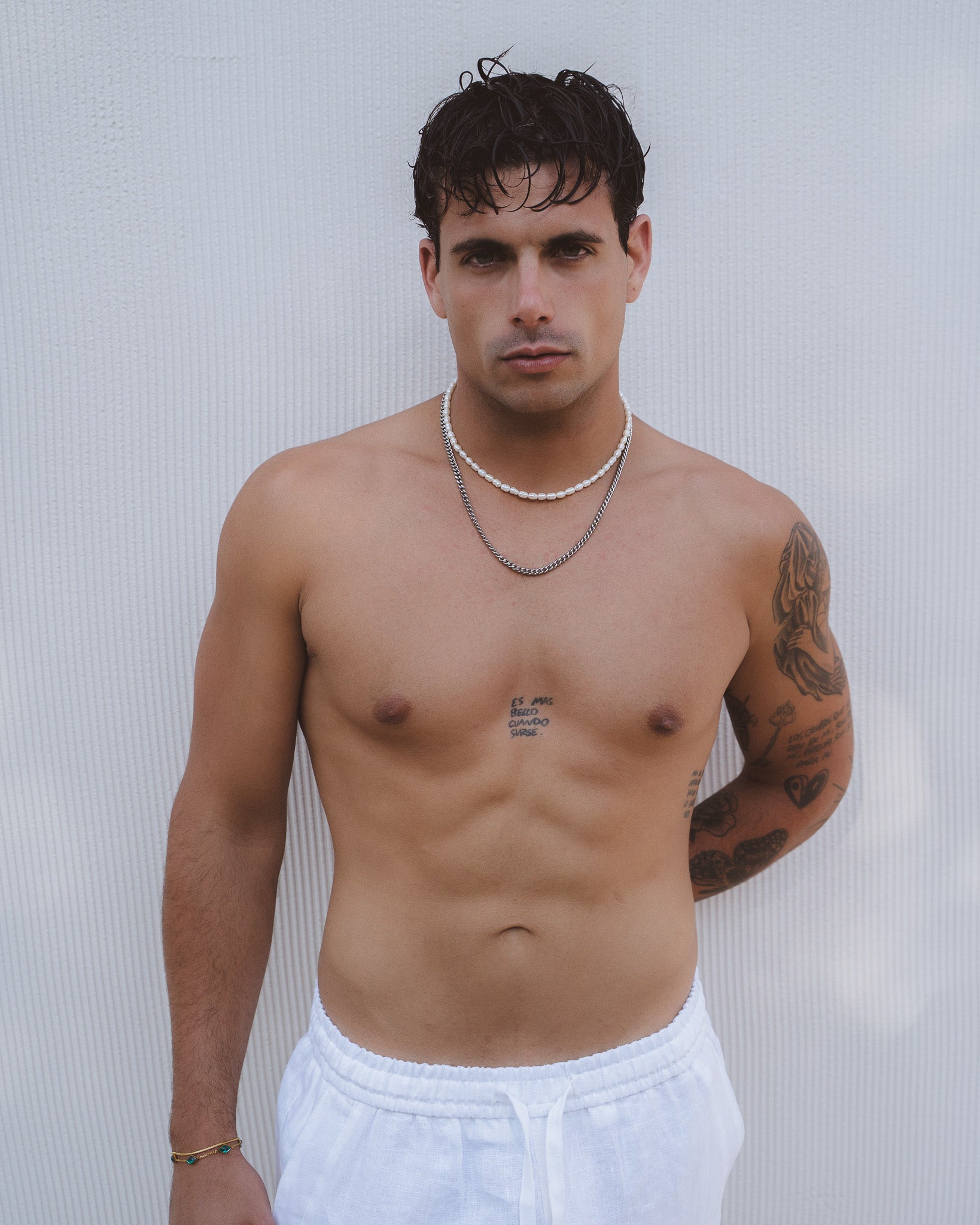 Man wearing a Belize Pearl Chain double strand white freshwater pearls with a silver chain against a pale background