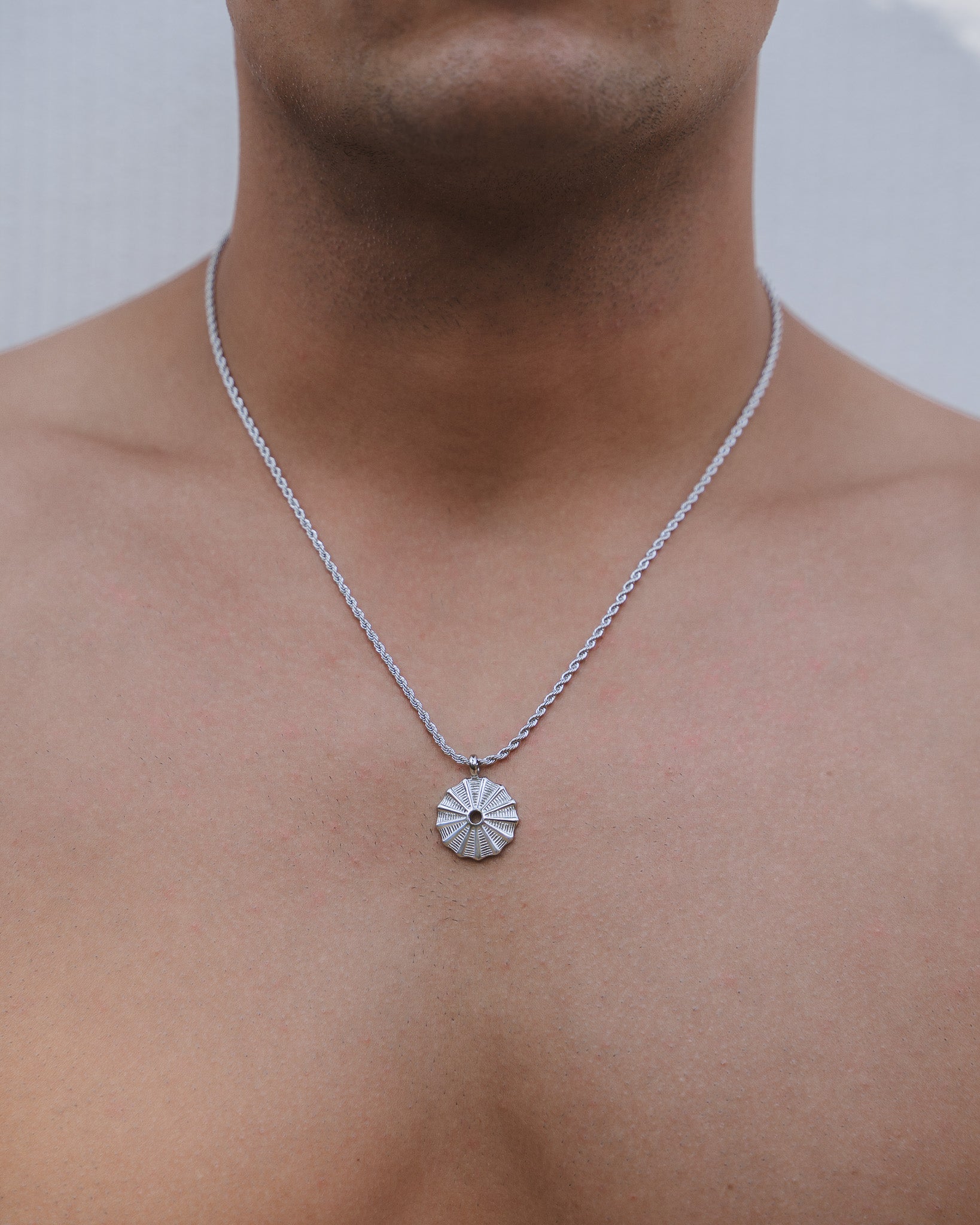 Silver rope chain necklace with a round sunburst pendant resting on the chest.