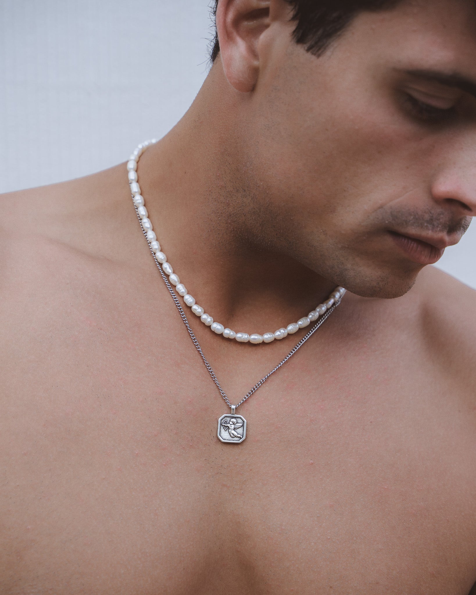 Cupid pendant necklace paired with a white pearl strand and silver chain on the neck.