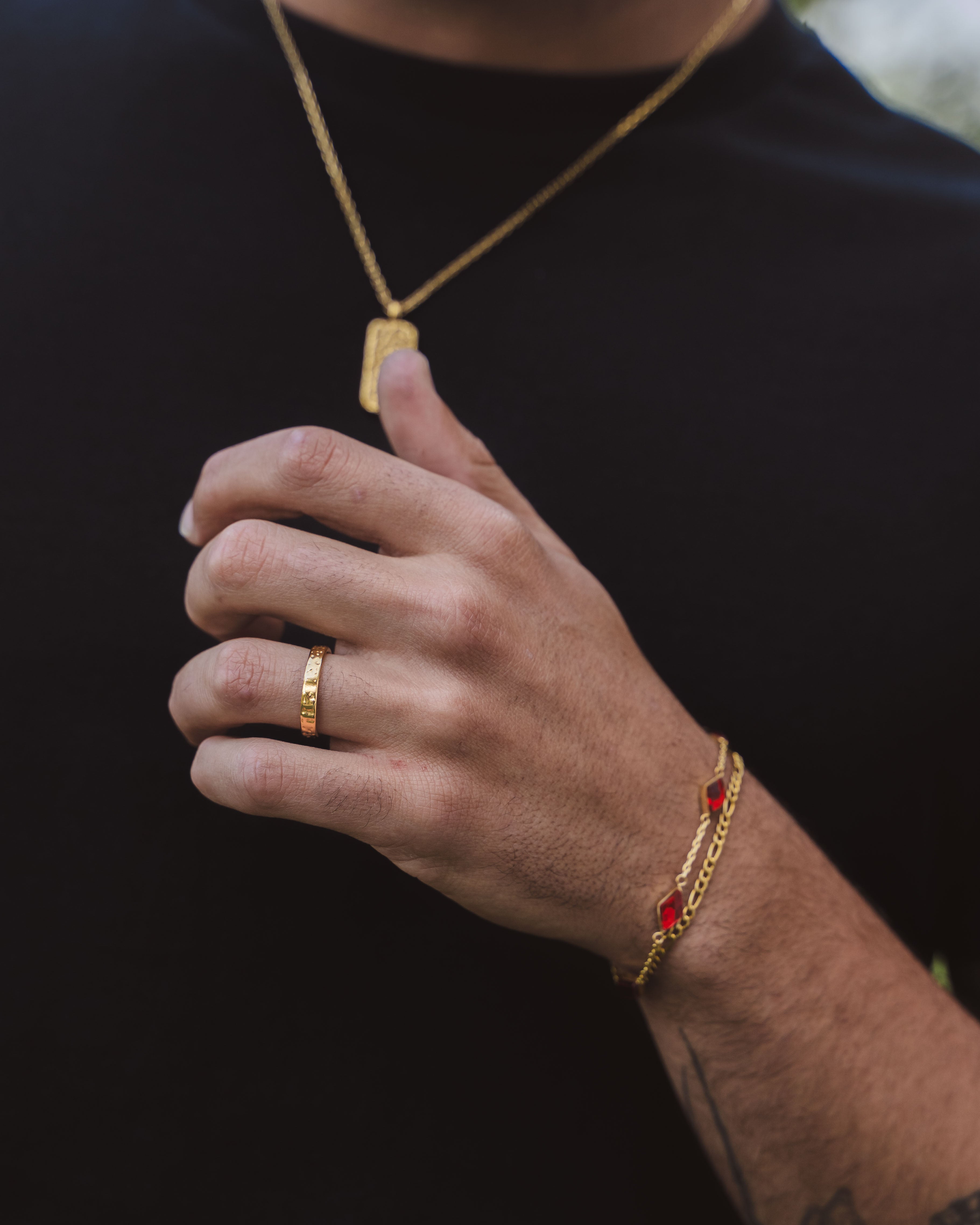 Person wearing a hammered gold pendant necklace along with a textured ring and a red gemstone bracelet