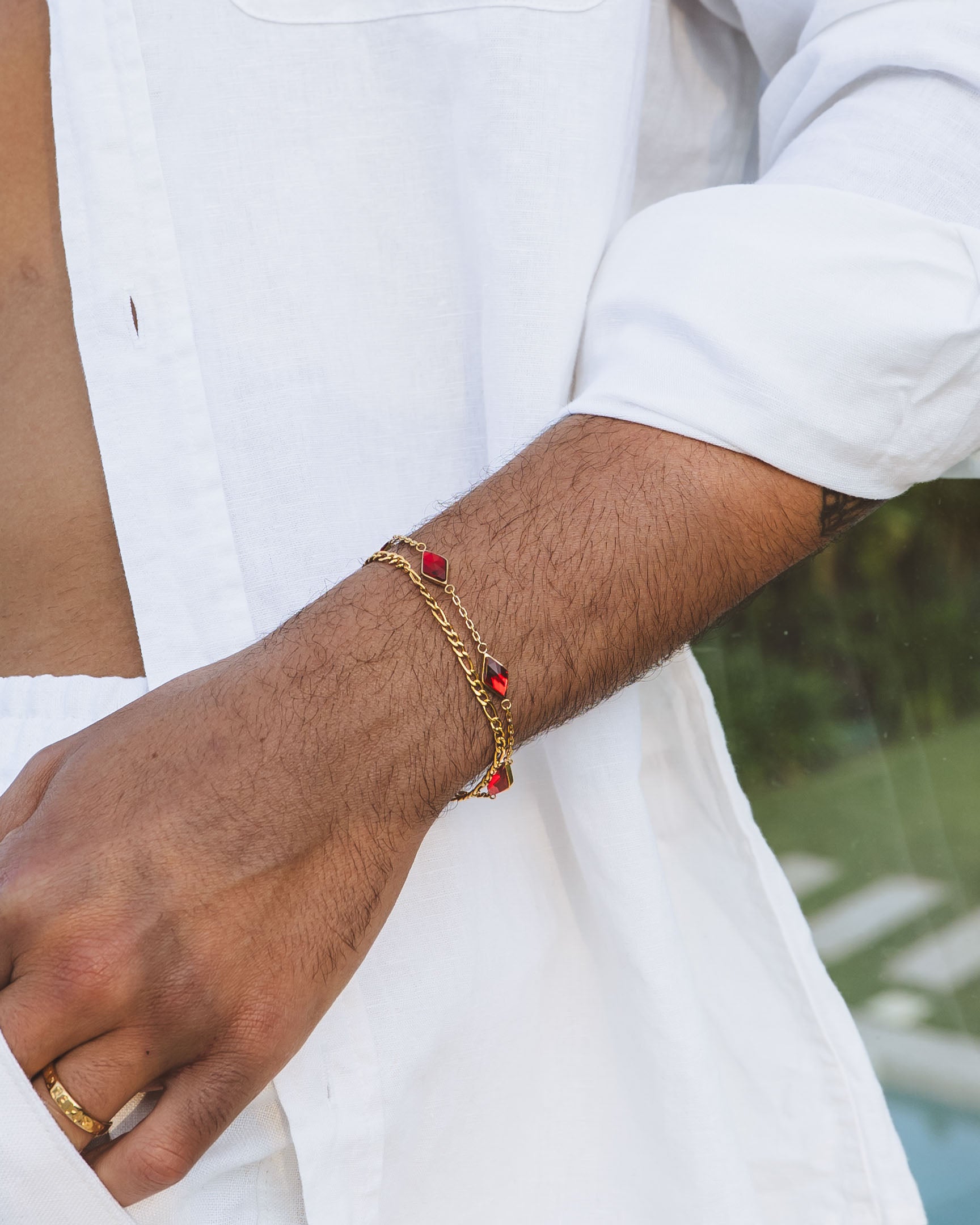 Delicate Amberes gold bracelet with red gemstone links on a man's wrist over a white shirt