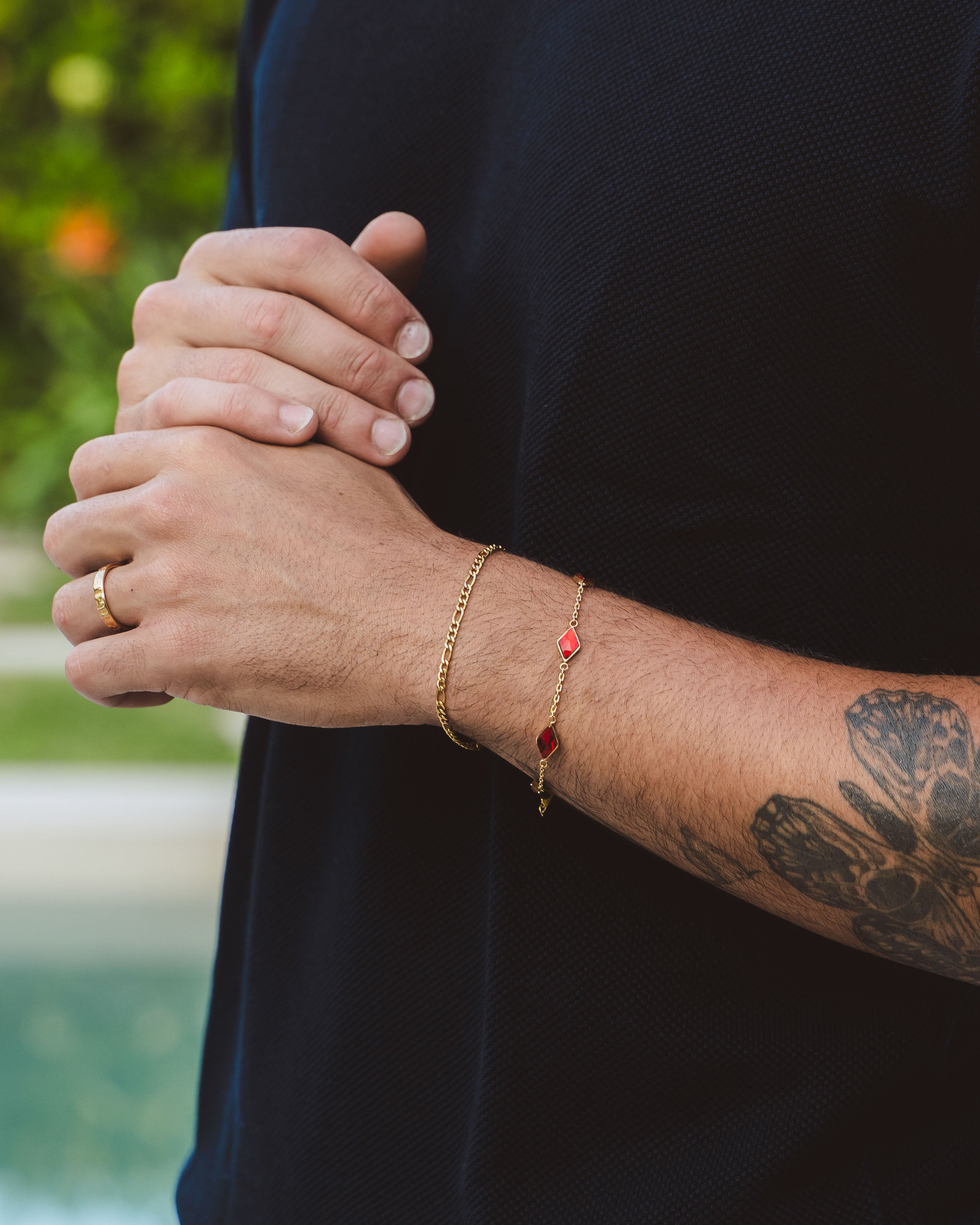 Close up of Amberes gold bracelet with red gemstone links on a man's wrist with a navy sleeve
